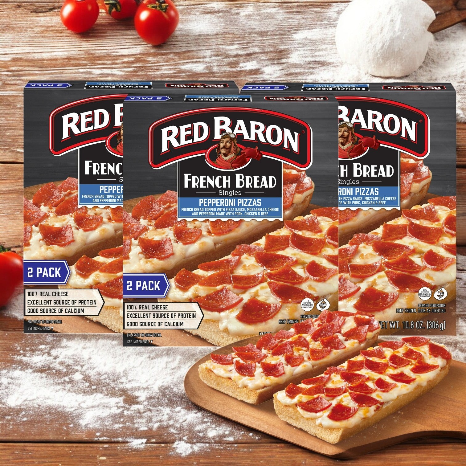 Three boxes of Red Baron Pepperoni French Bread Personal Frozen Pizza, 10.8 oz, are displayed on a wooden table with savory pepperoni and gooey mozzarella cheese. In front is a pizza ready to eat, set against a backdrop of flour and ripe tomatoes for a rustic look.