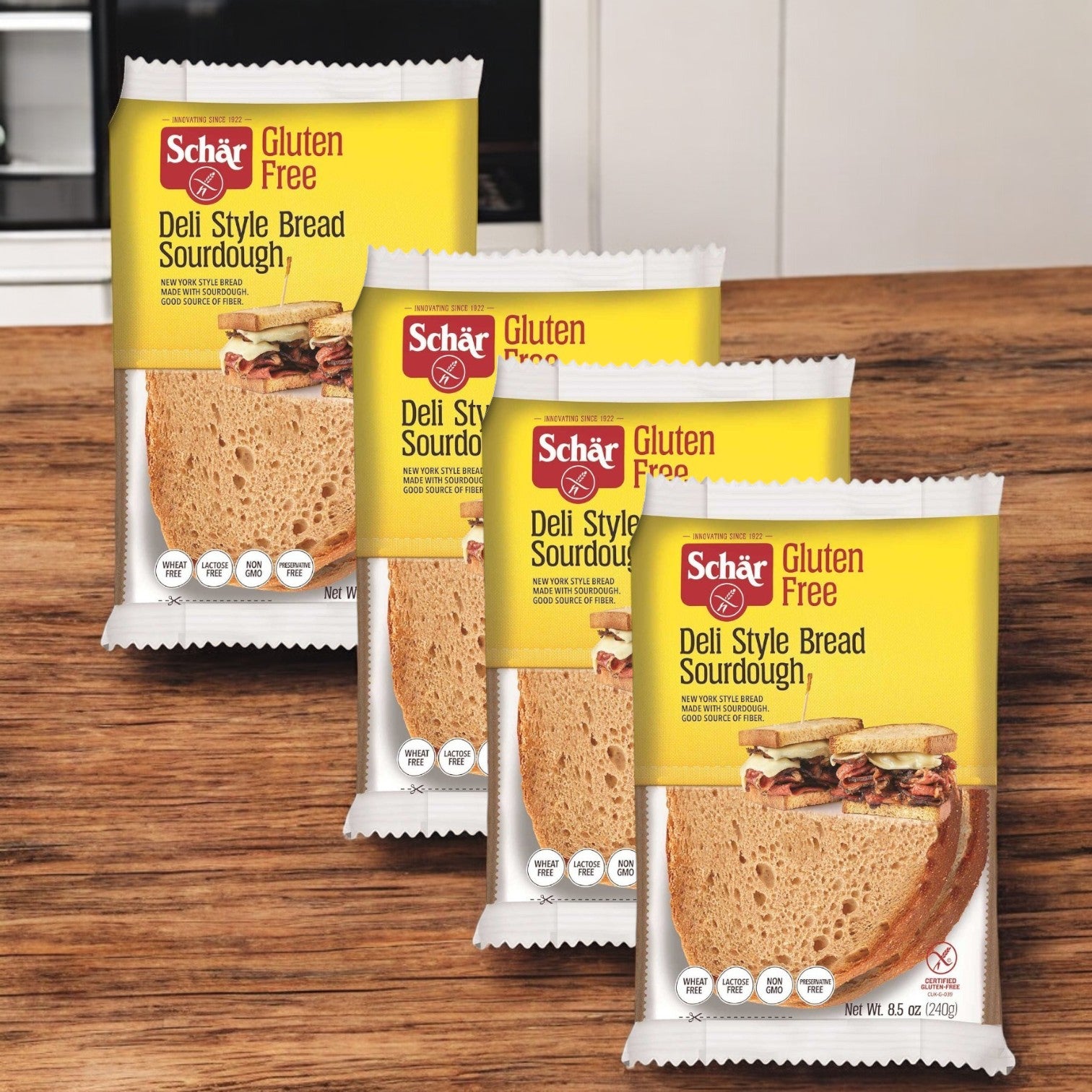 Four 8.5 oz. packages of Schar Gluten Free Deli Style Bread, known for its soft texture, are displayed on a wooden kitchen counter.