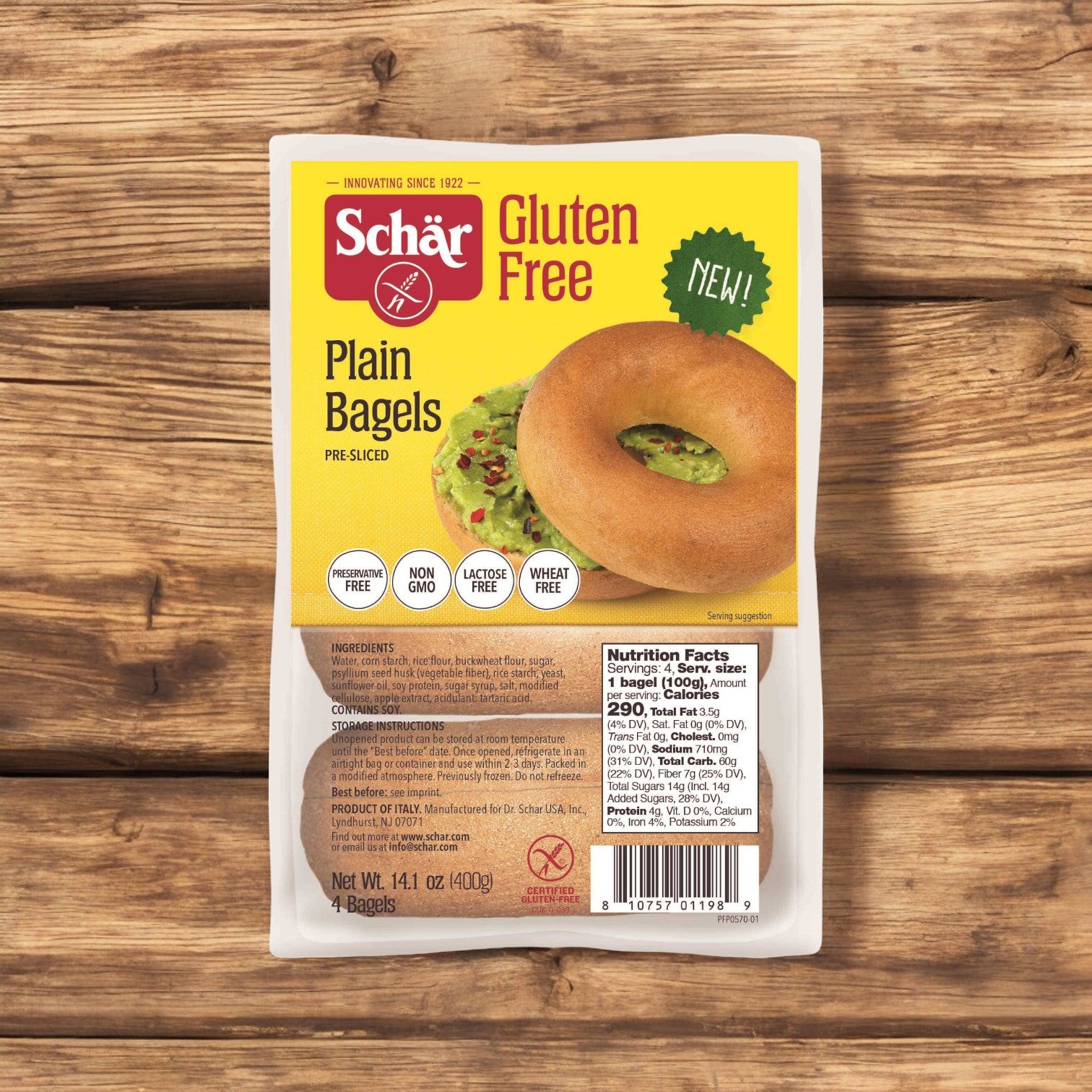 A package of Schar Gluten Free Plain Bagel, 14.1 oz. - 4 per case, is placed on a wooden surface, highlighting its deli-style bread qualities. The packaging emphasizes benefits such as being non-GMO, lactose-free, and wheat-free, crafted with premium gluten-free ingredients.