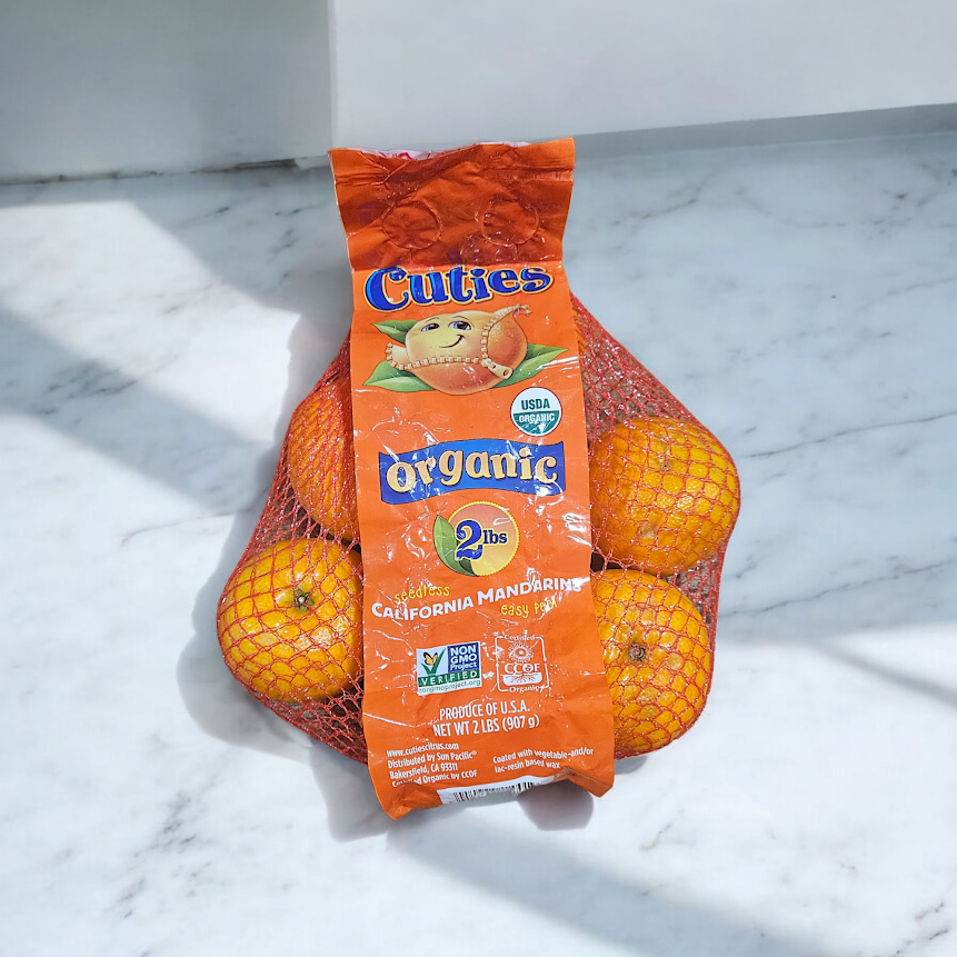 A 2-pound bag of Cuties Organic California mandarins, packed with Vitamin C, rests on a marble countertop in a red mesh bag.