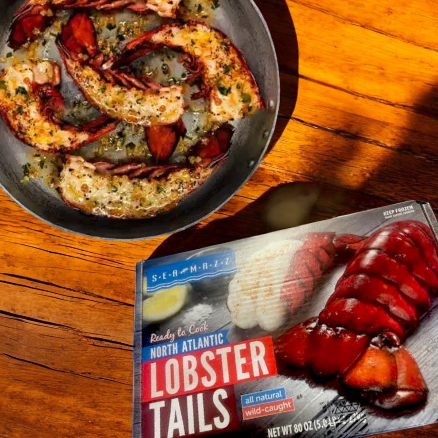 Cooked, sustainably sourced North Atlantic Lobster Tails from Sea Mazz beside a Seamazz Ready to Cook North Atlantic Lobster Tails 5-pound box on a wooden surface.