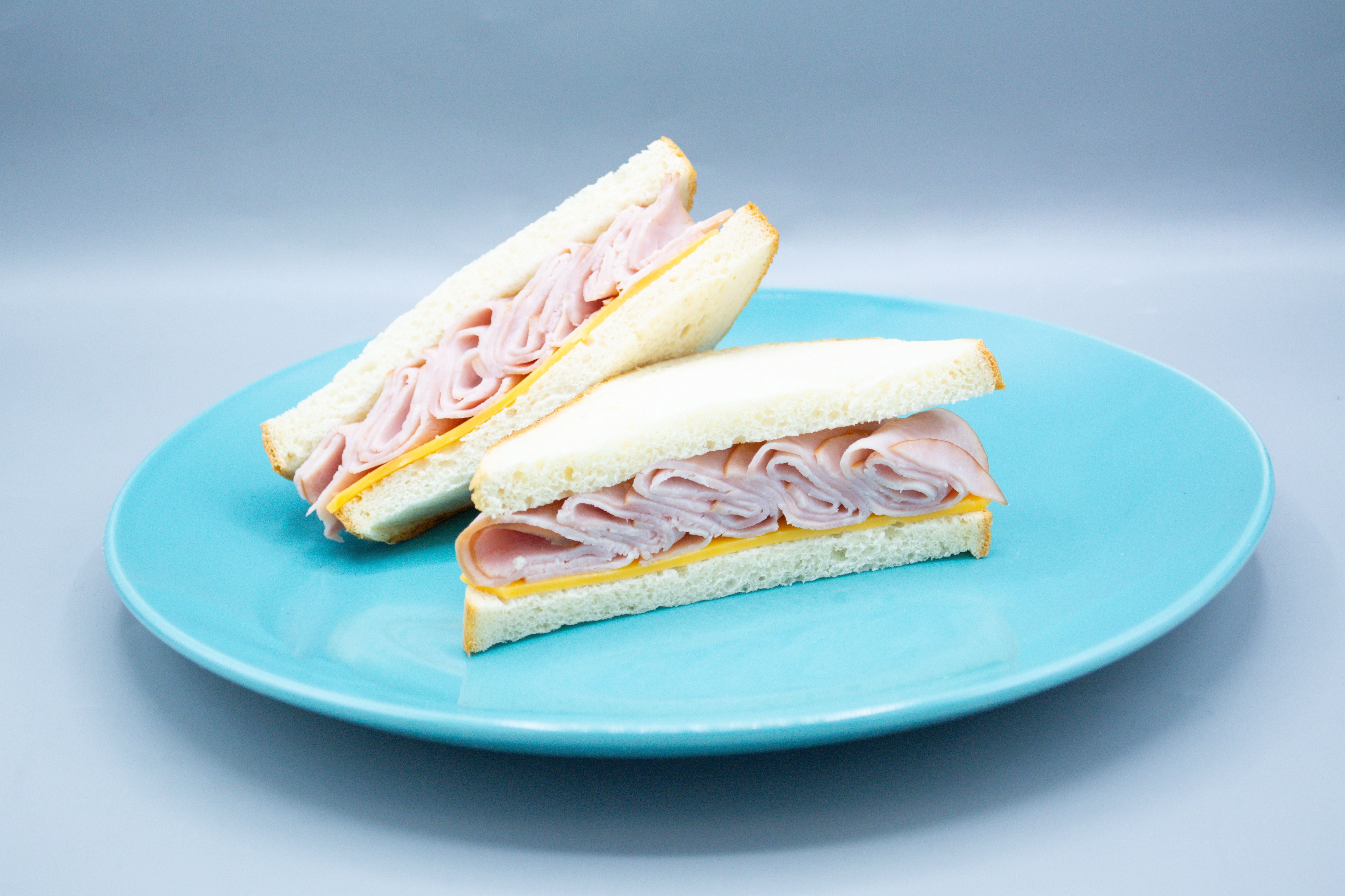 Two halves of a Taylor Farms Turkey and Cheddar Sandwich on white bread are placed on a blue plate, with the layers of turkey and cheese clearly visible.