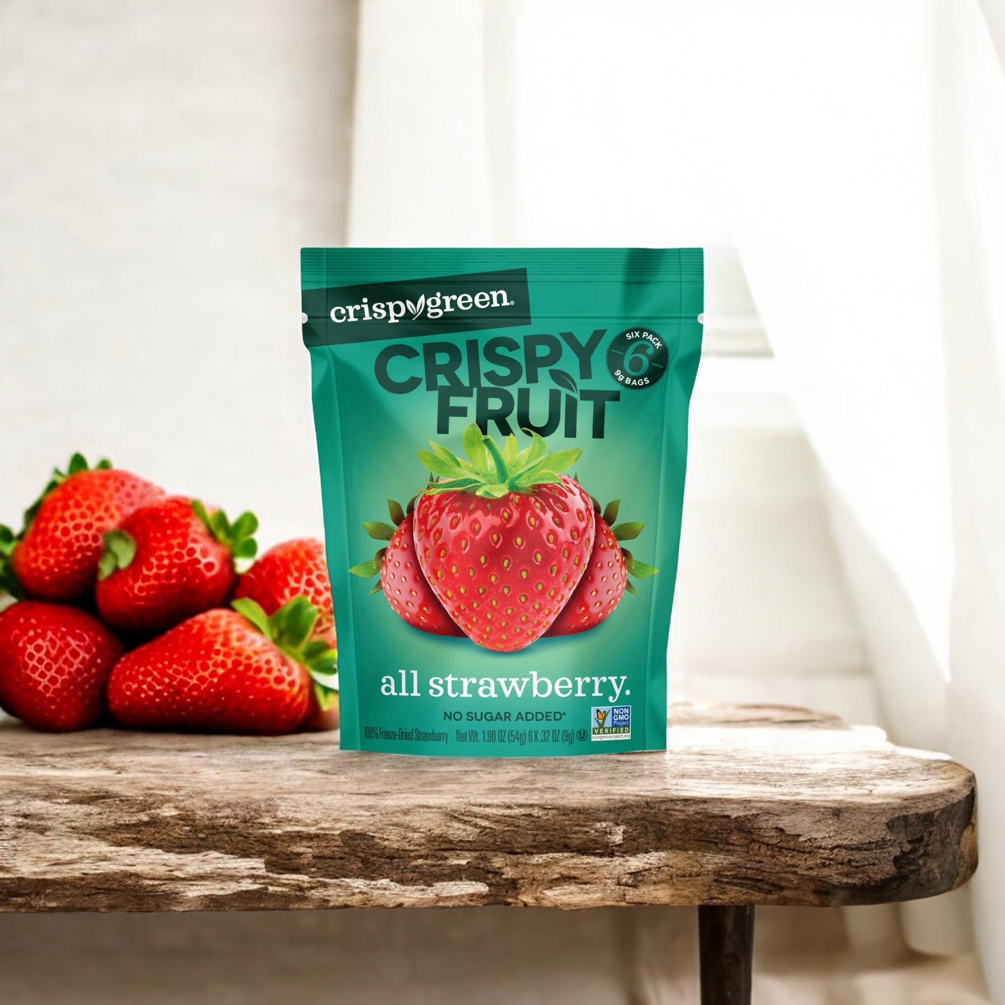 A packet of Crispy Fruit Freeze-Dry Strawberry - 0.35 oz - 1 Count is showcased on a wooden surface beside fresh strawberries, with a white curtain in the background. Savor the natural sweetness of this guilt-free indulgence anytime, courtesy of Crispy Fruit.