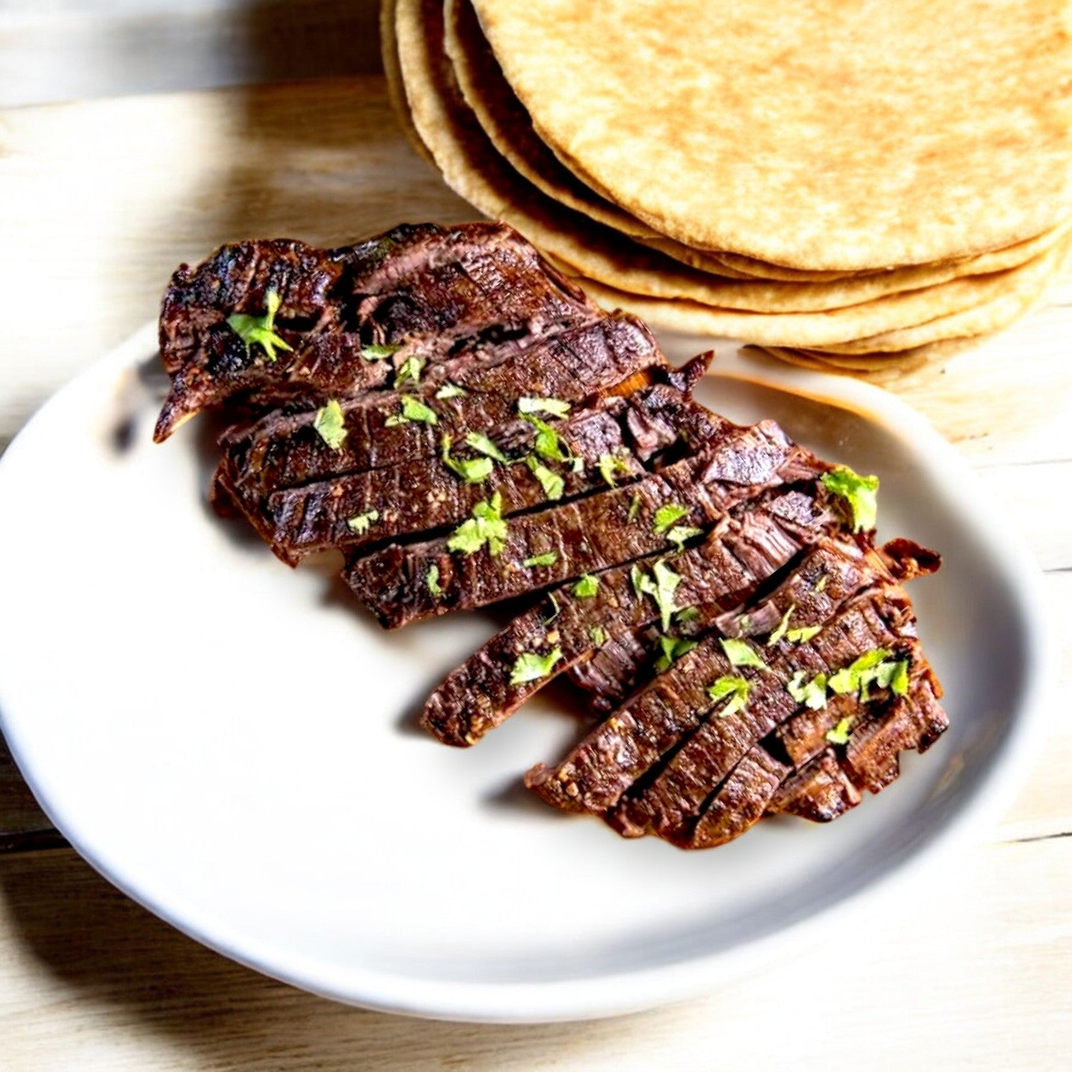 Mino Prime Steaks' quality skirt steak strips are expertly grilled, garnished with fresh herbs, and elegantly presented on a white plate with a stack of tortillas.