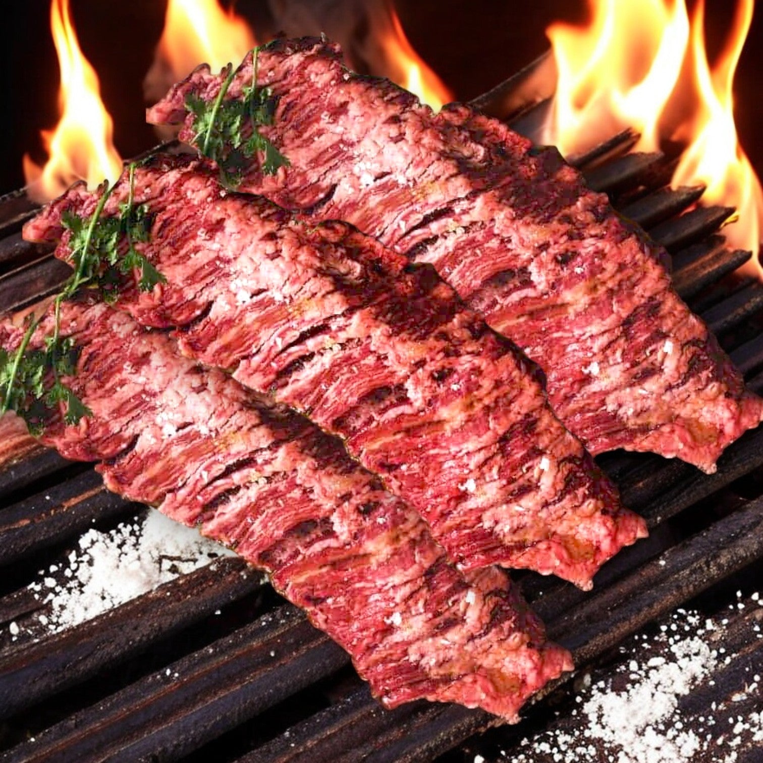 Three Mino Prime Steaks skirt steaks sizzle on a flaming barbecue grill, showcasing their premium quality.