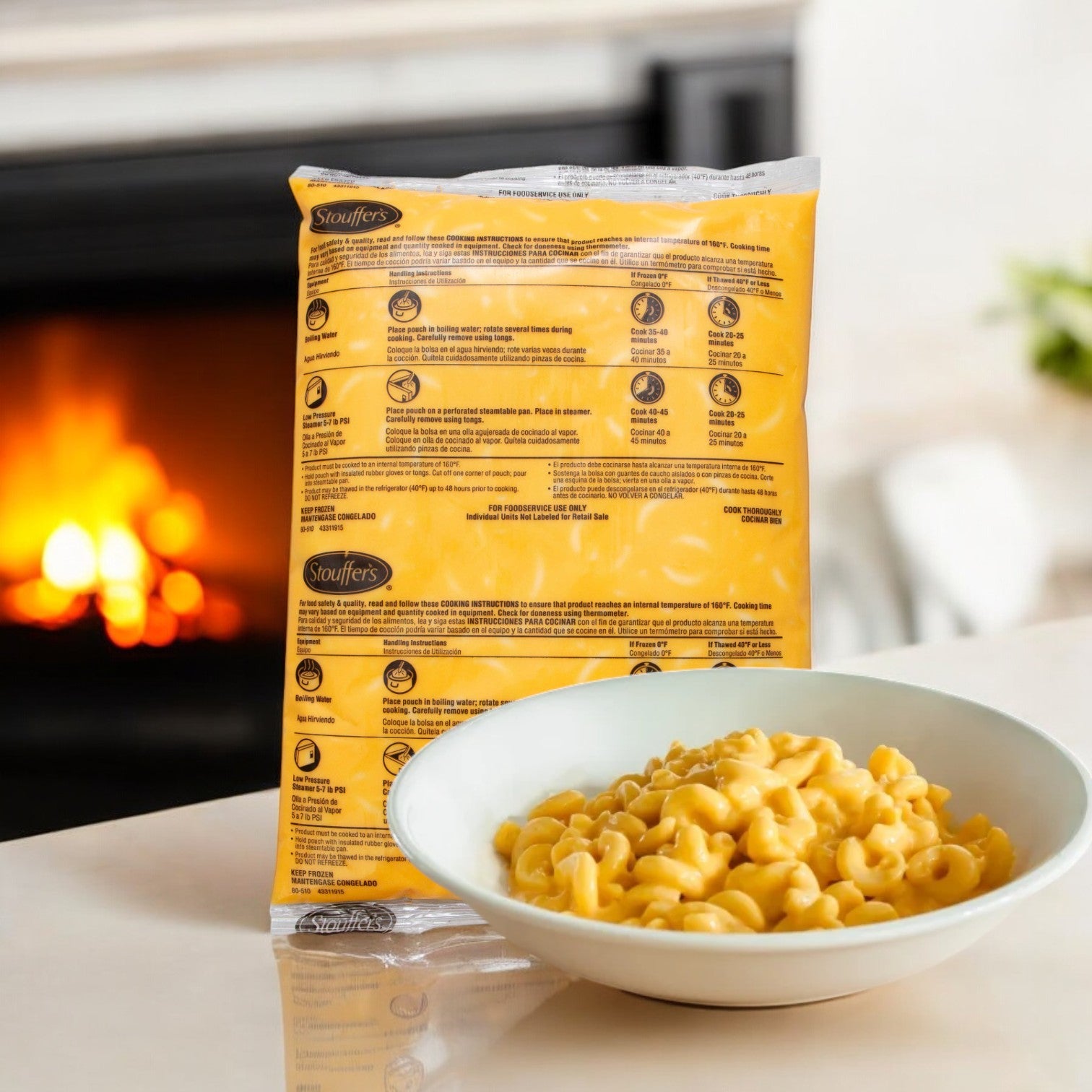 A steaming bowl of Stouffer's family-sized macaroni and cheese sits invitingly on the table by the fireplace, while a large package of Stouffer's Entree Macaroni And Cheese Pouch, 80 oz. - 1 Case, 4 Pack, boasting its use of high-quality ingredients, awaits in the background.