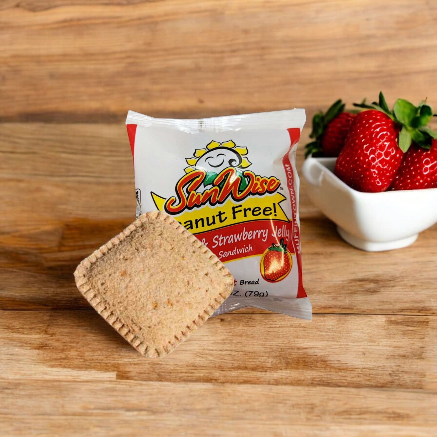 A 96-case SunWise SunButter and Strawberry Jelly Sandwich pack with an unwrapped sandwich in front and a small bowl of strawberries placed beside it on a wooden surface.