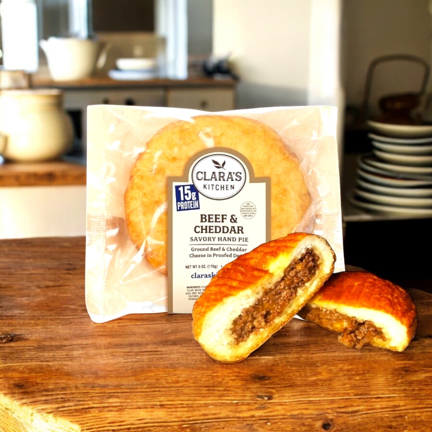 Clara's Kitchen Beef & Cheddar Handpie – 6 oz., an ideal quick meal, is showcased on a wooden table with a sliced pie and kitchen items in the background.