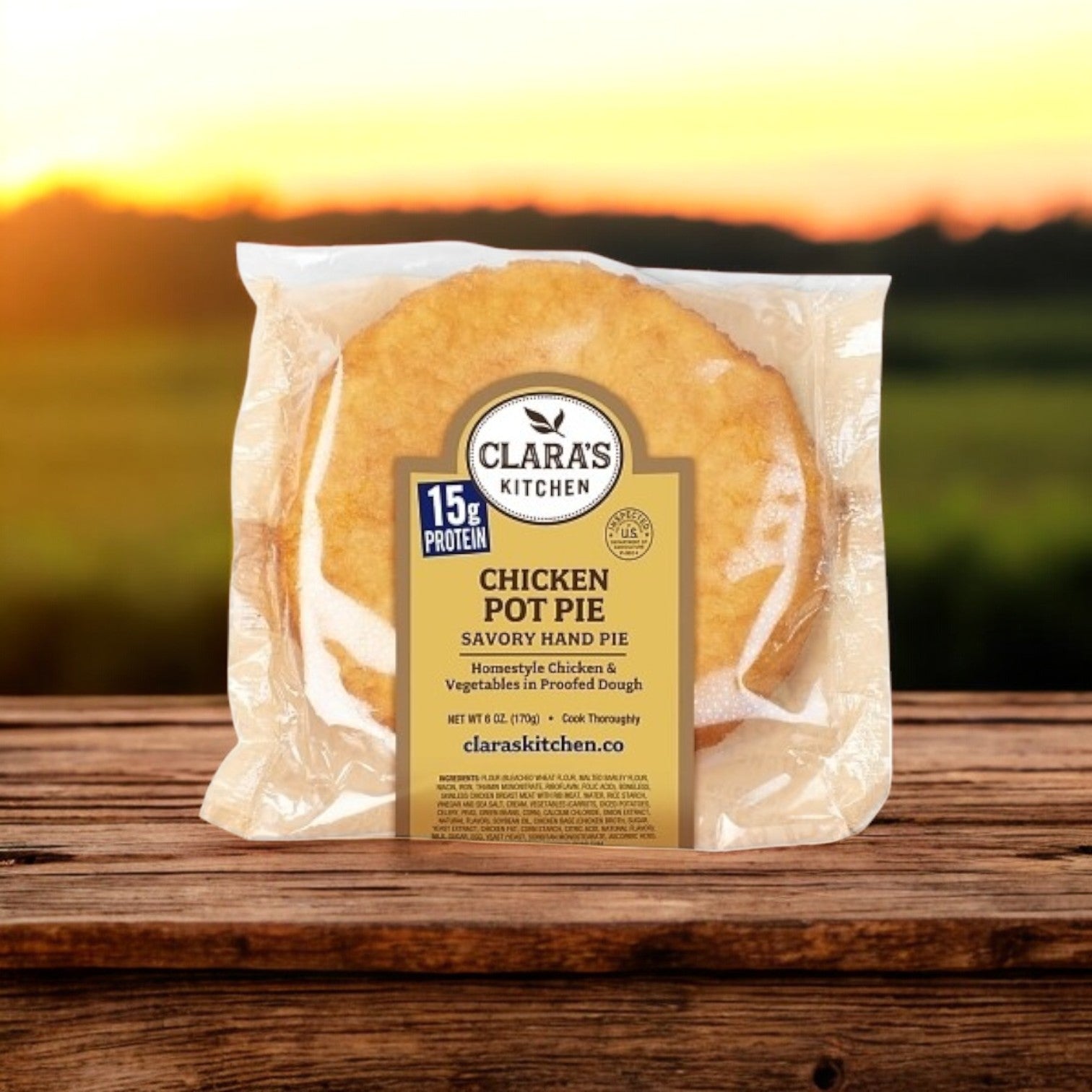 Clara’s Kitchen Hand-Held Chicken Pot Pie offers 15g of protein and is set on a wooden surface, with a blurred outdoor sunrise or sunset backdrop emphasizing its balance of flavor and convenience. Enjoy this comfort food from Clara's Kitchen as the perfect meal solution.
