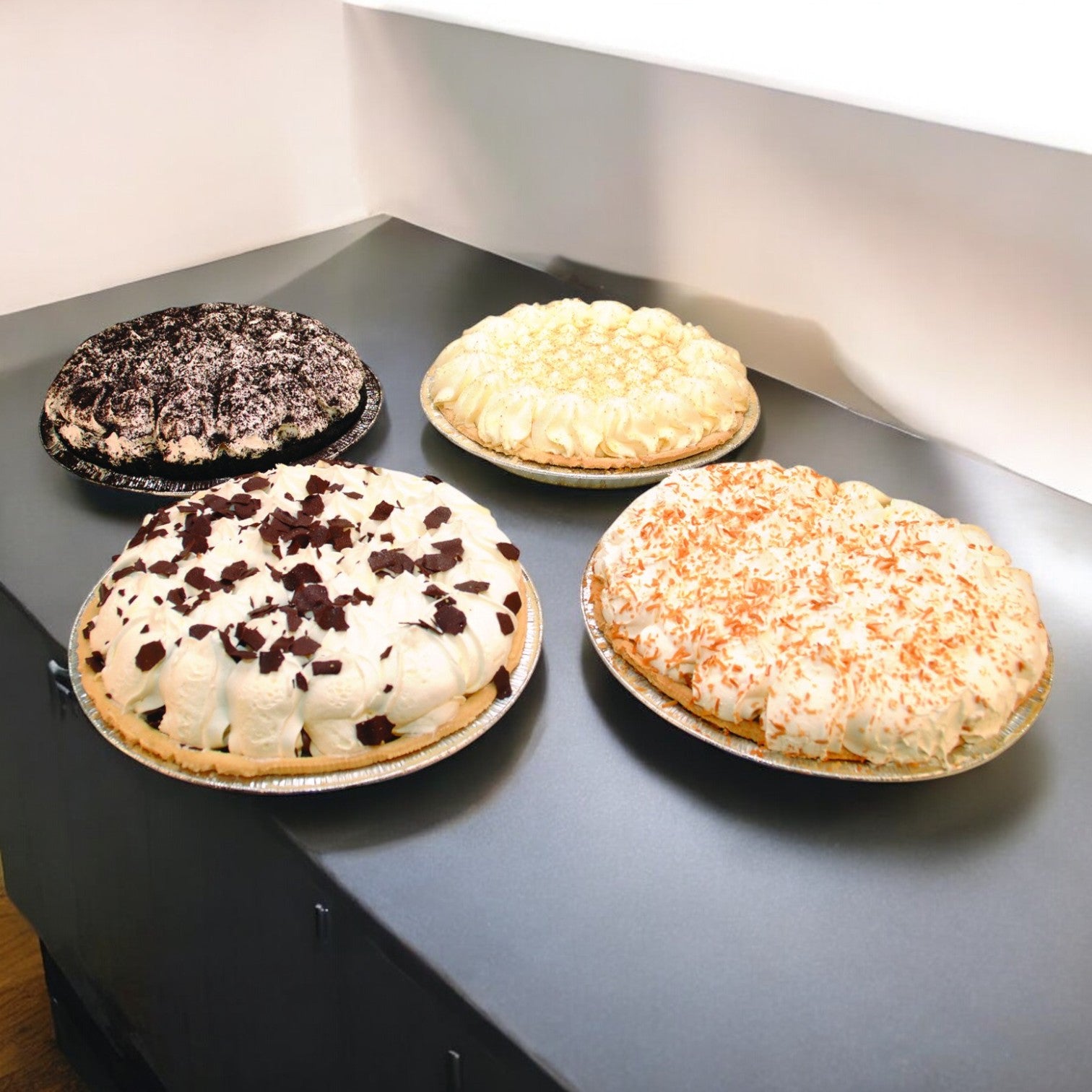 Four Sysco Imperial assorted cream pies, each 10", are arranged on a counter, offering decadent desserts with toppings like chocolate shavings, coconut flakes, and delightful crumbled toppings.