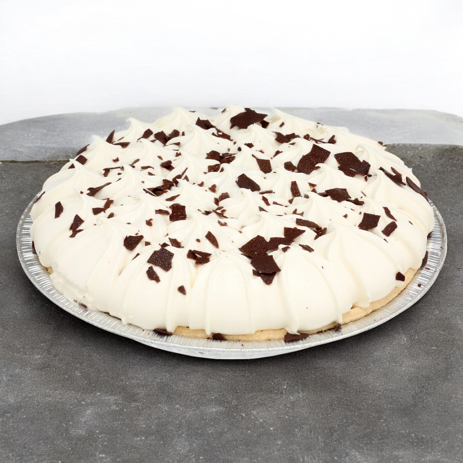 This decadent Sysco Imperial Assorted Cream Pie features a rich filling topped with delicate chocolate shavings, elegantly presented in a silver tin on a gray surface.