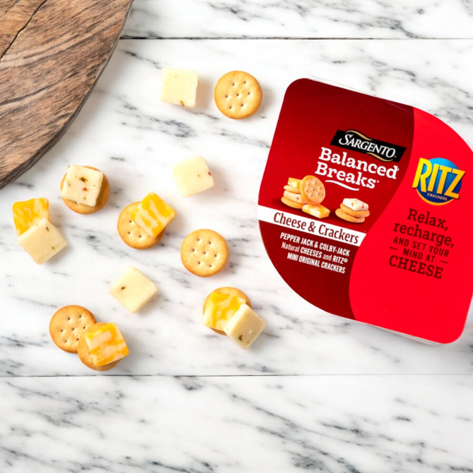 A package of Sargento Balanced Breaks Cheese and Crackers is open on a marble surface, with some cheese and crackers scattered nearby.