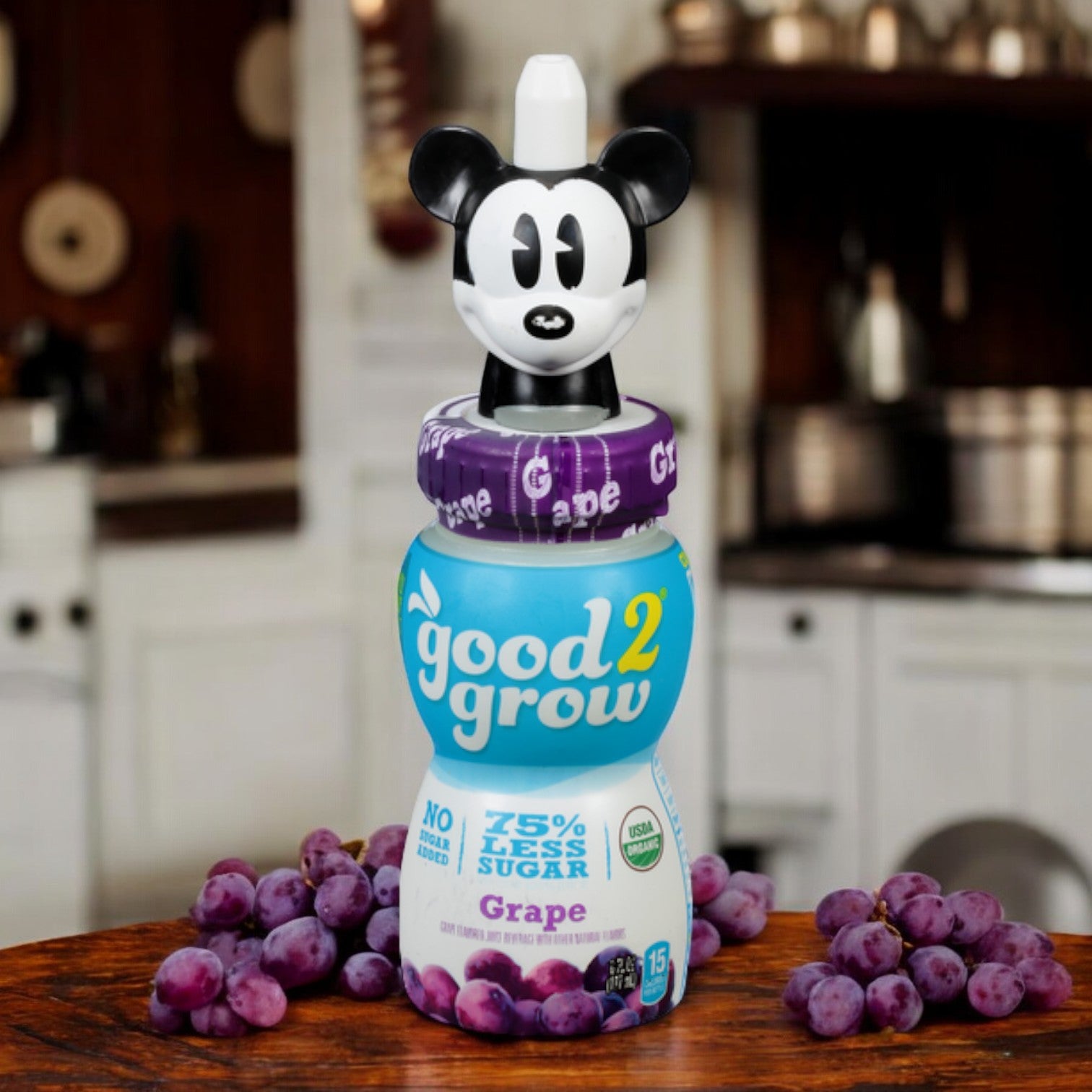 A 6 oz bottle of Good2grow Grape Juice Single Serve from Easy Lunches, featuring a unique collectible character top and displayed in a kitchen setting with grapes. The label proudly states it has 75% less sugar and contains 100% real grape juice.