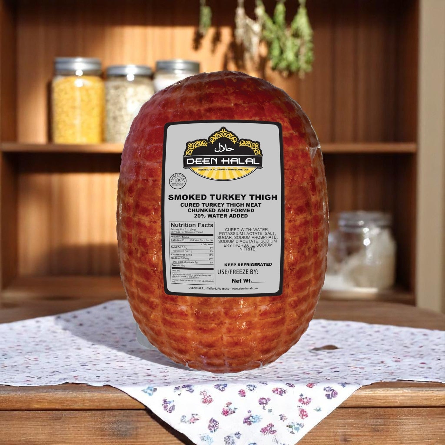 A Deen Halal Smoked Turkey Thigh labeled with the Deen Halal brand rests on a patterned tablecloth, with shelves of jars in the background.