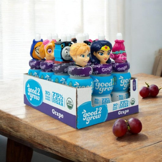 A case of Easy Lunches' Good2Grow Single Serve Grape Juice, featuring 6 fluid ounce bottles with a variety of collectible character tops, sits on a wooden table next to two plums, showcasing the delight of natural ingredients.