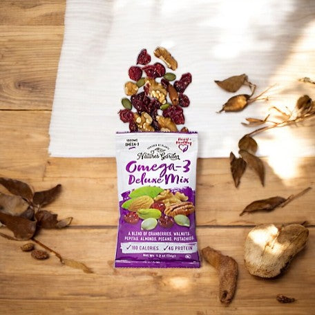 A packet of Nature Garden Trail Mix Omega-3 containing cranberries, walnuts, almonds, pecans, and pistachios is open on a wooden table, with some of the heart-healthy mix spilled out.