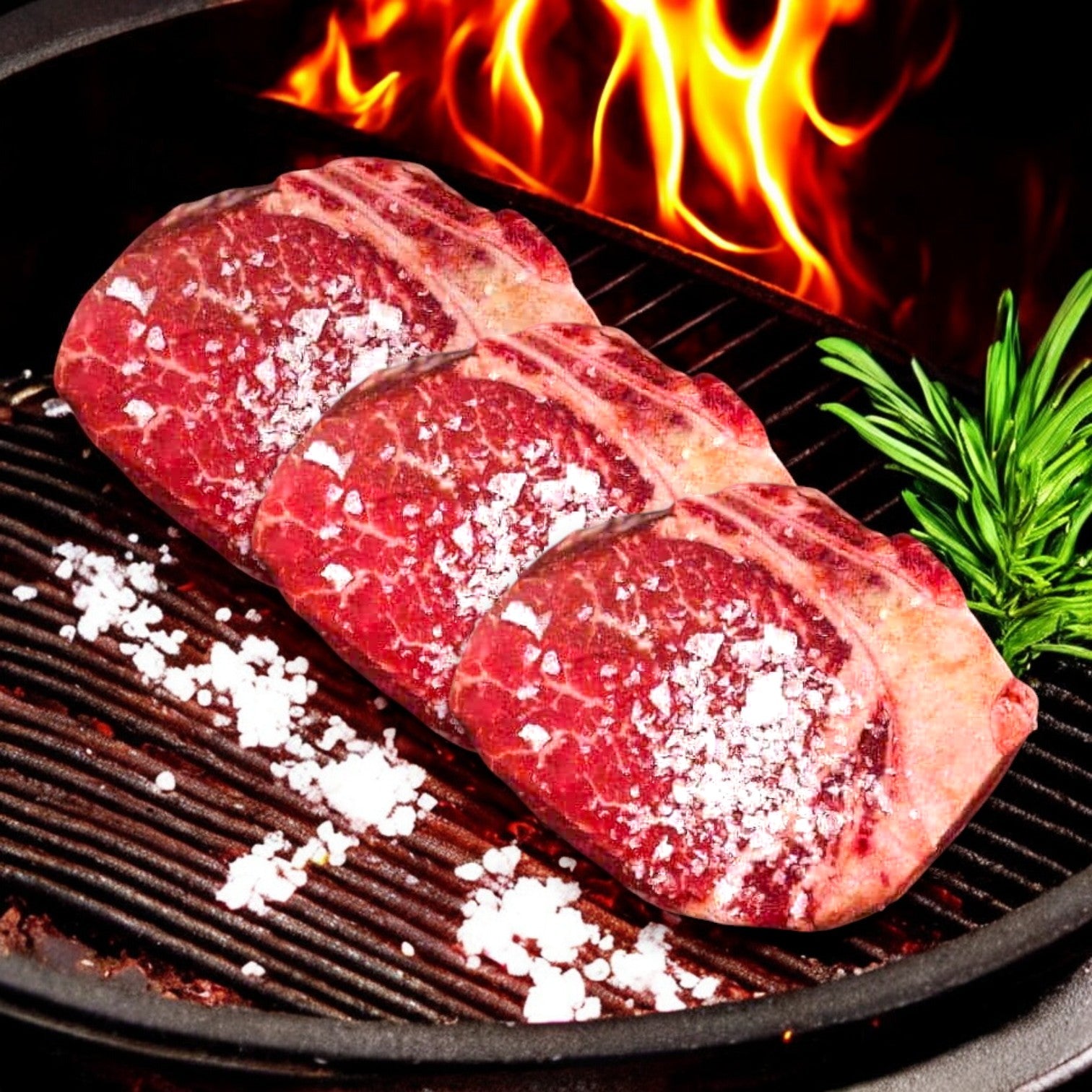 The Gambatese" Bone-In Filet from Mino Prime Steaks sizzling with salt on a grill, flames dancing, and a sprig of rosemary beside.