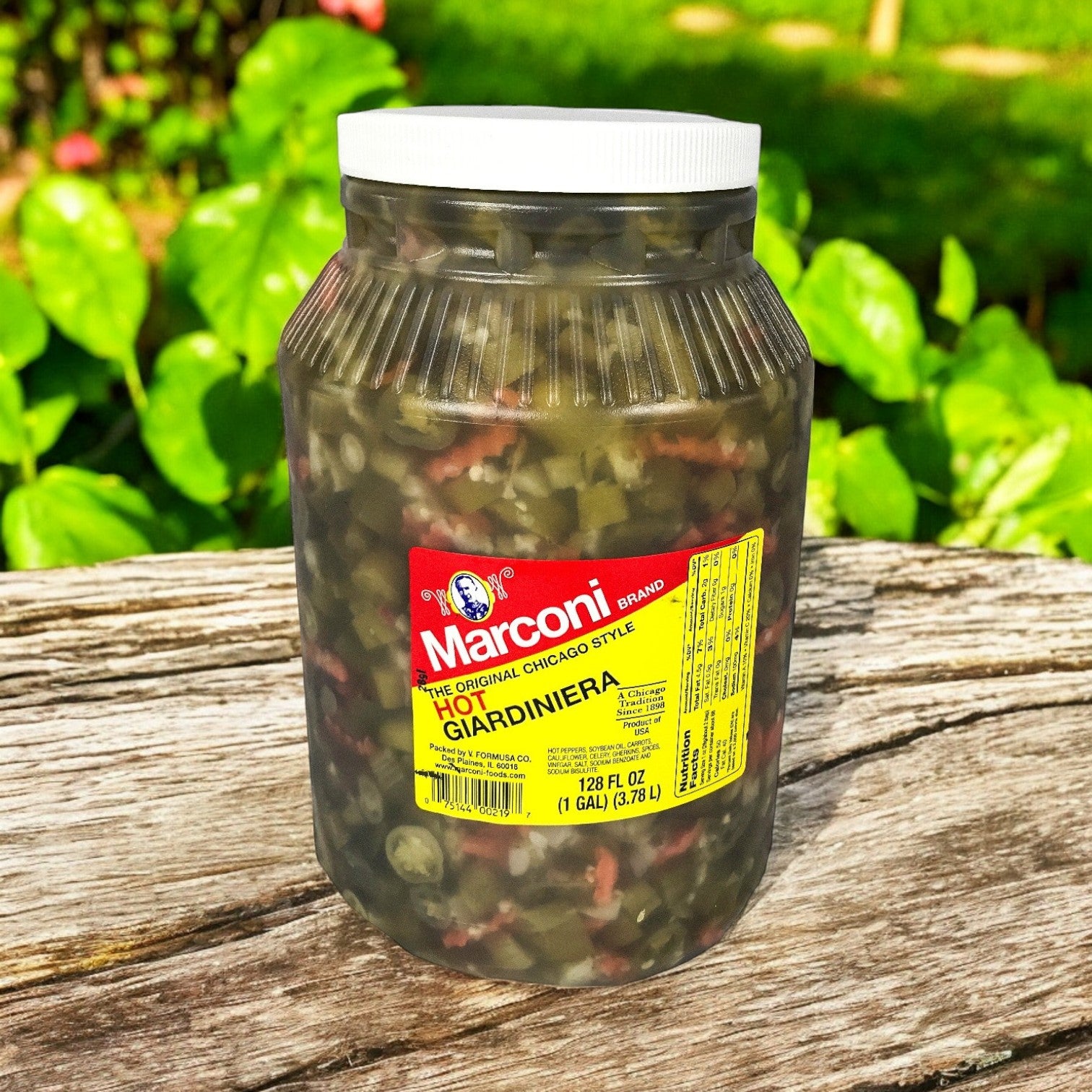 A 1-gallon jar of Marconi Giardiniera Hot by Marconi Foods, showcasing Italian-style pickled vegetables, is placed on a wooden surface outdoors.