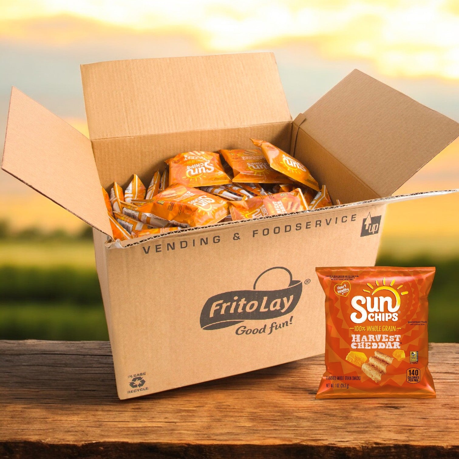 A cardboard box of Sun Chips' Sunchips Multi-Grain Harvest Cheddar Chips 104/1 oz sits on wood, displaying its cheesy flavor, while a whole grain-rich bag stands upright beside it.