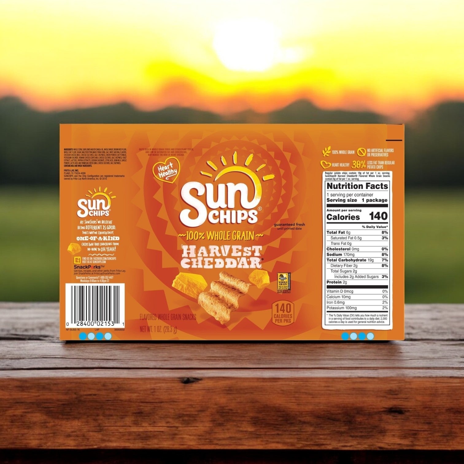 A box of Sun Chips Multi-Grain Harvest Cheddar Chips rests on a wooden surface with a sunset backdrop, highlighting its cheesy taste, nutritional details, and the wholesome benefits of whole grains.