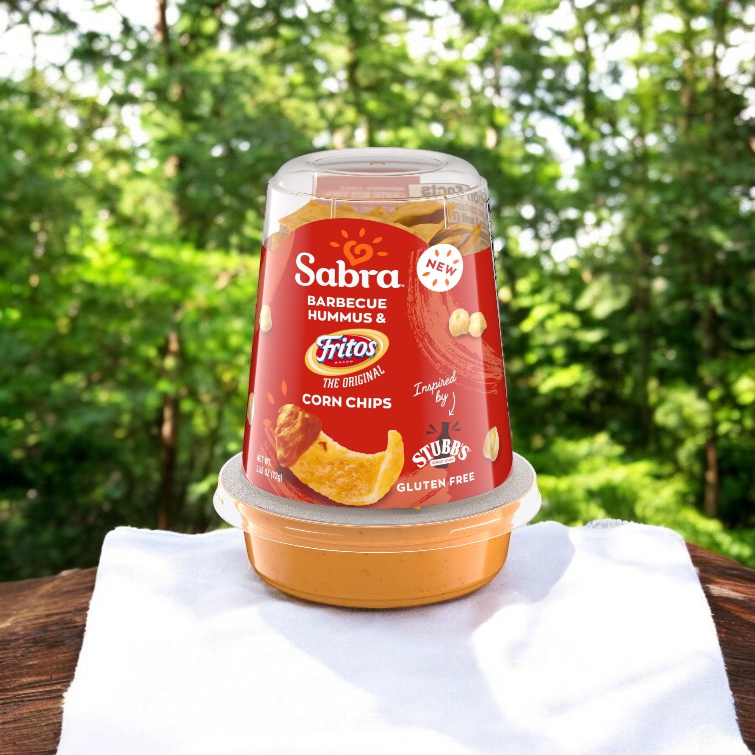 An 8-pack of Sabra BBQ Hummus Dip with Fritos (2.55 oz each) rests on a wooden surface with a white cloth, making for the ideal portable snack.