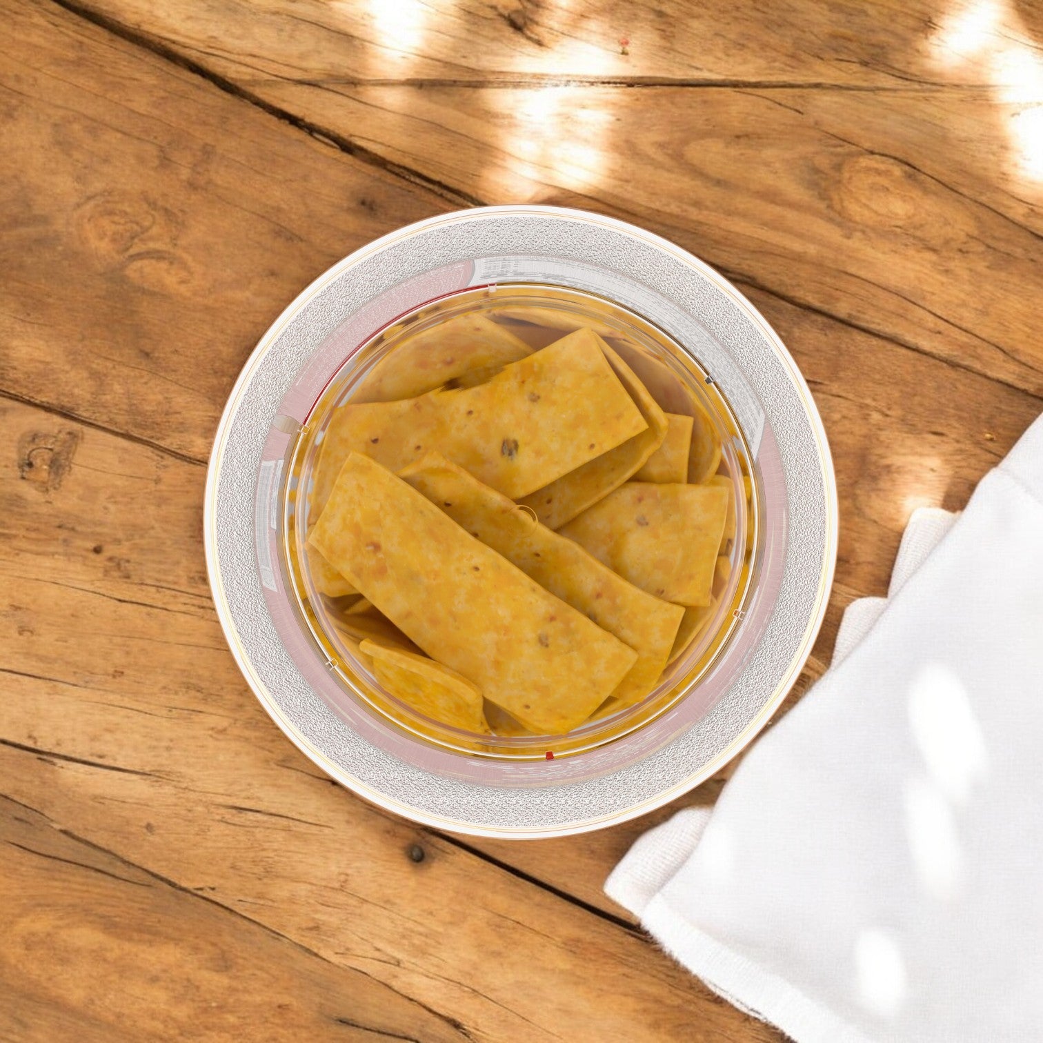 On a wooden table, a bowl of rectangular crackers and pretzels is served with a white napkin and paired with Sabra BBQ Hummus Dip with Fritos for a delightful snack.