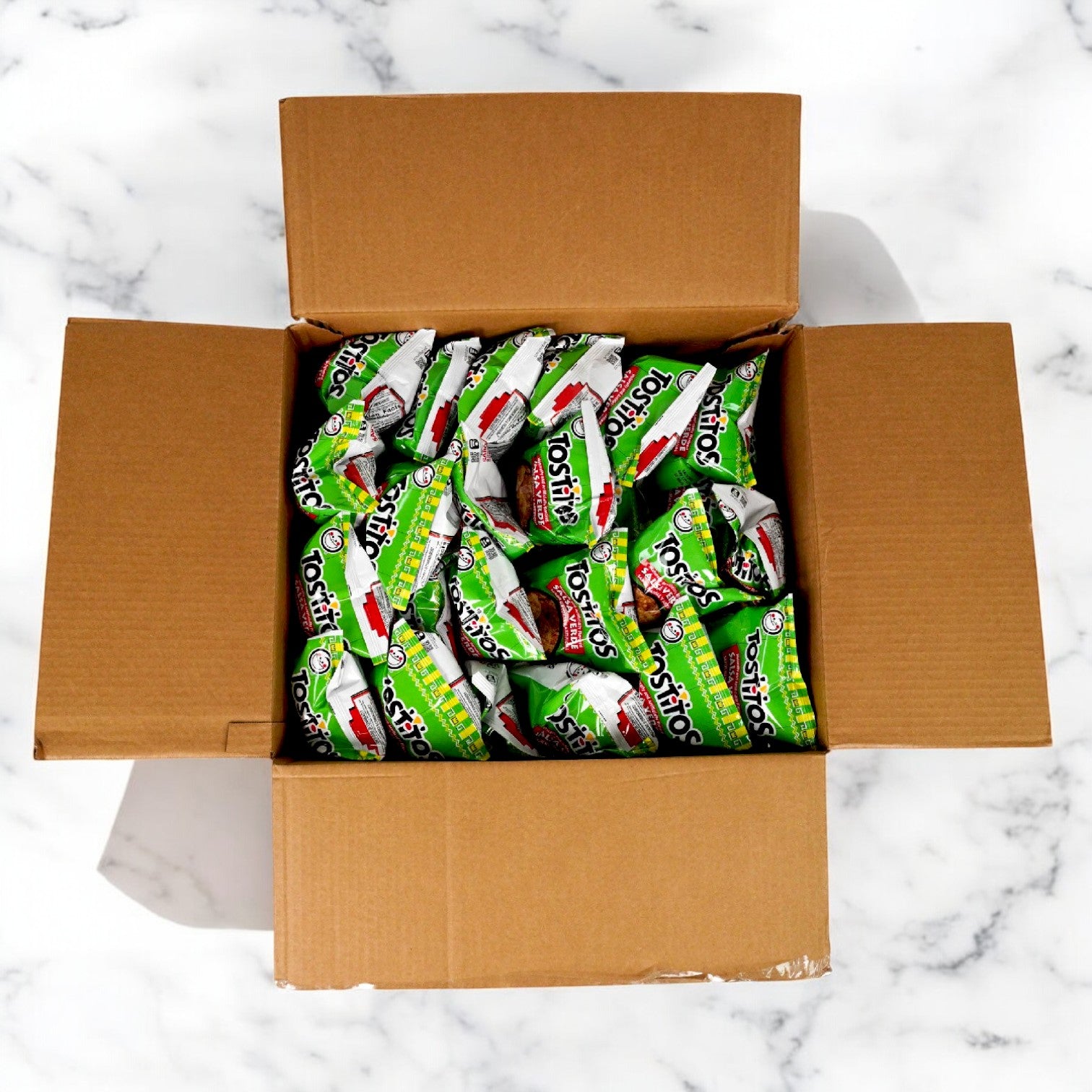 A cardboard box filled with Tostitos Salsa Verde Tortilla Rounds - 28 Pack (2.63 oz each) sits on a marble surface, presenting snacks that promise a burst of flavor in every crunch.