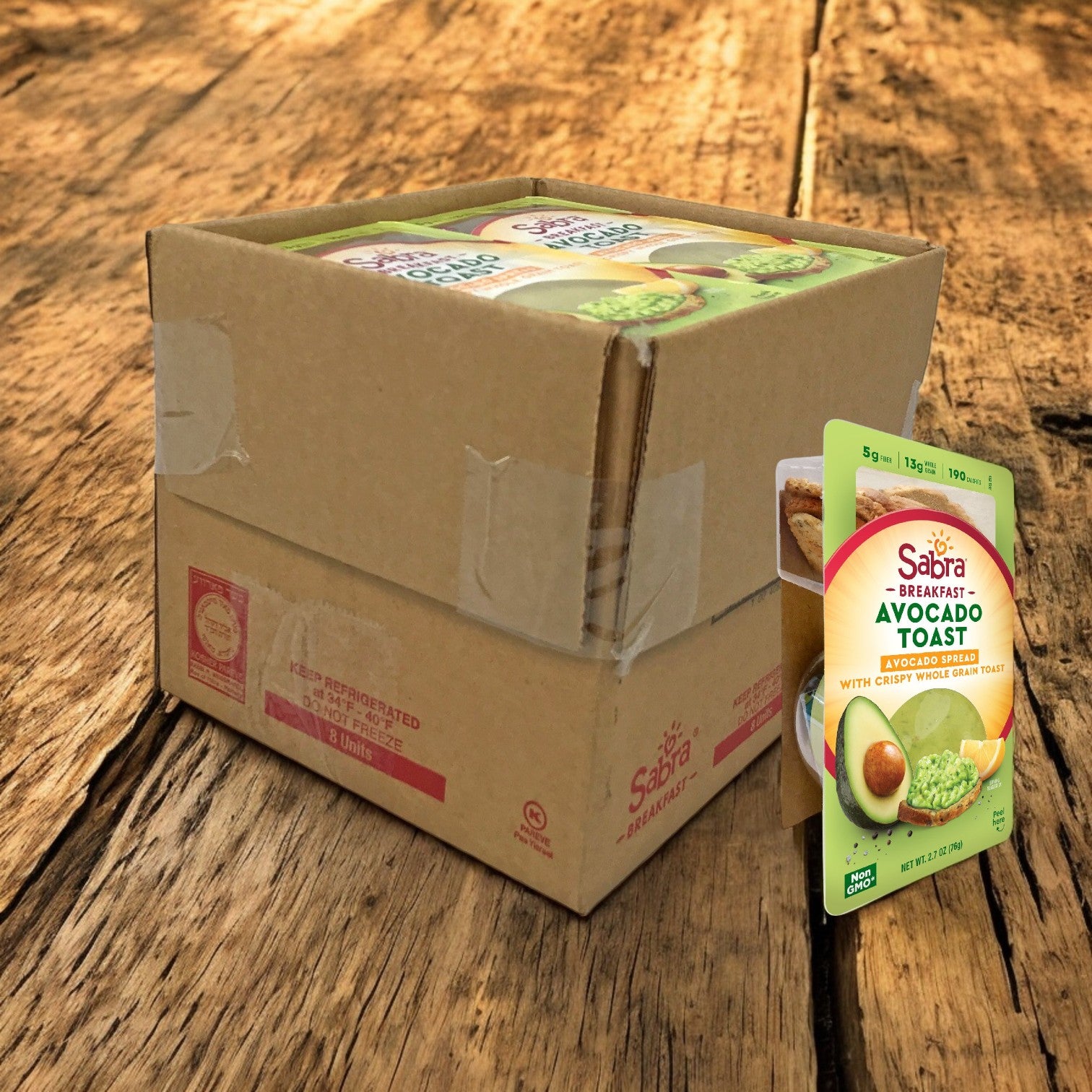 A box of Sabra Avocado Chunky Spread with Toast, 8 Count, 2.7 oz each, rests on a wooden surface, showcasing one upright package. Each serving offers a creamy blend made with high-quality ingredients to kickstart your day.