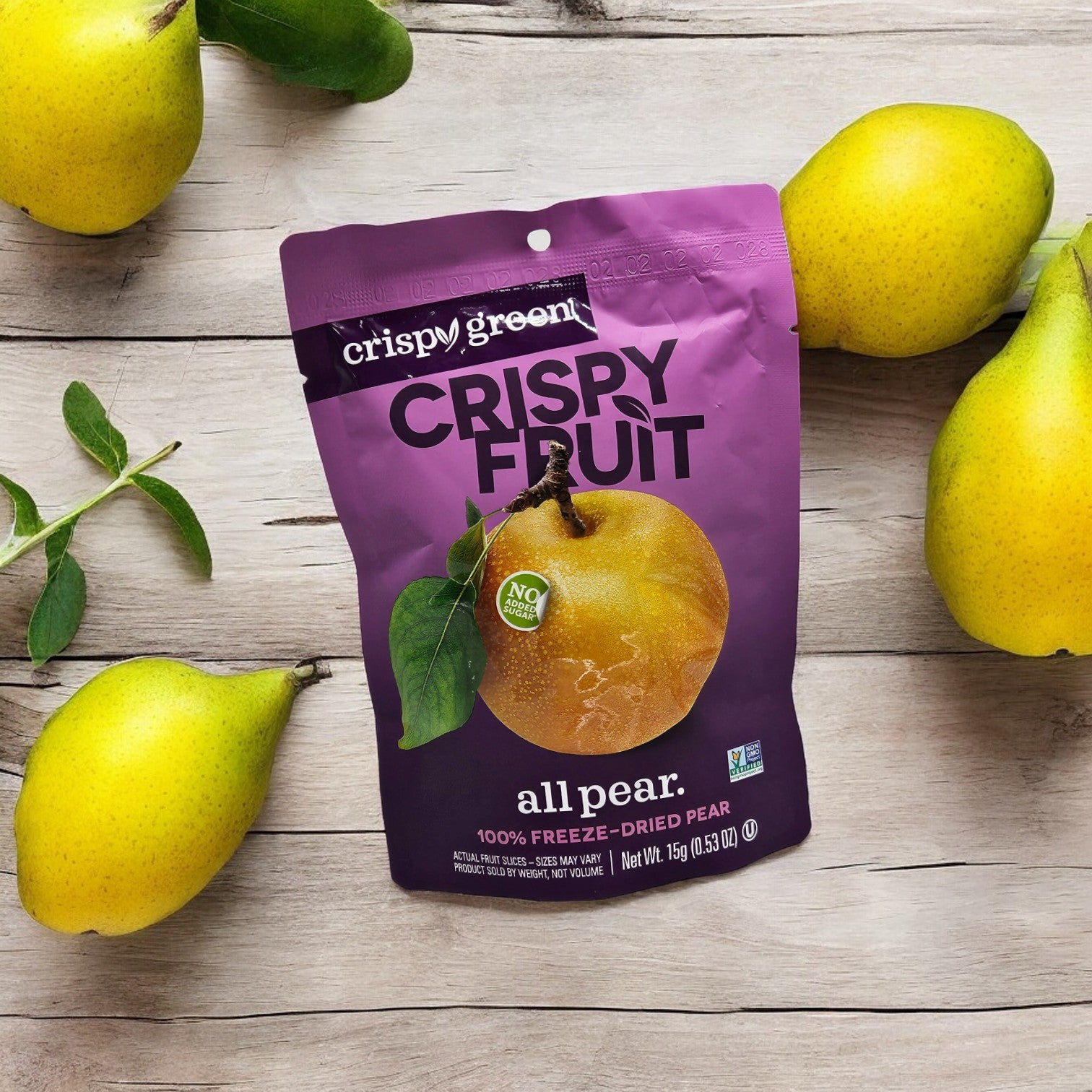 A packet of Crispy Green Crispy Fruit All Pear dried fruit snack (0.35 oz) is placed on a wooden surface surrounded by fresh pears, showcasing their commitment to sustainable production.