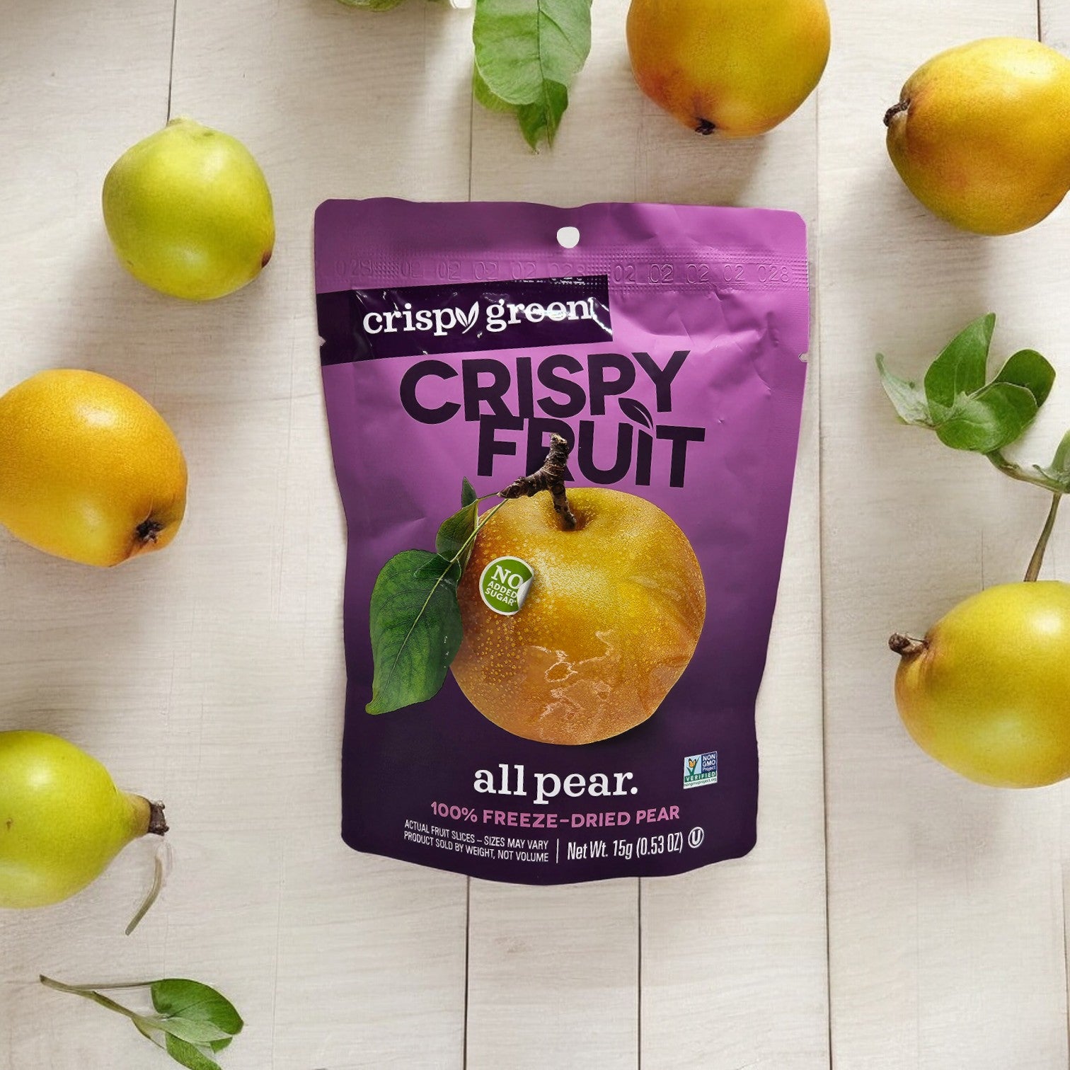 A bag of Crispy Green Crispy Fruit All Pear (0.35 oz, 1 count) placed on a white wooden surface, surrounded by fresh pears, alongside a package of Crispy Green Pineapple Slices showcasing sustainable production methods.