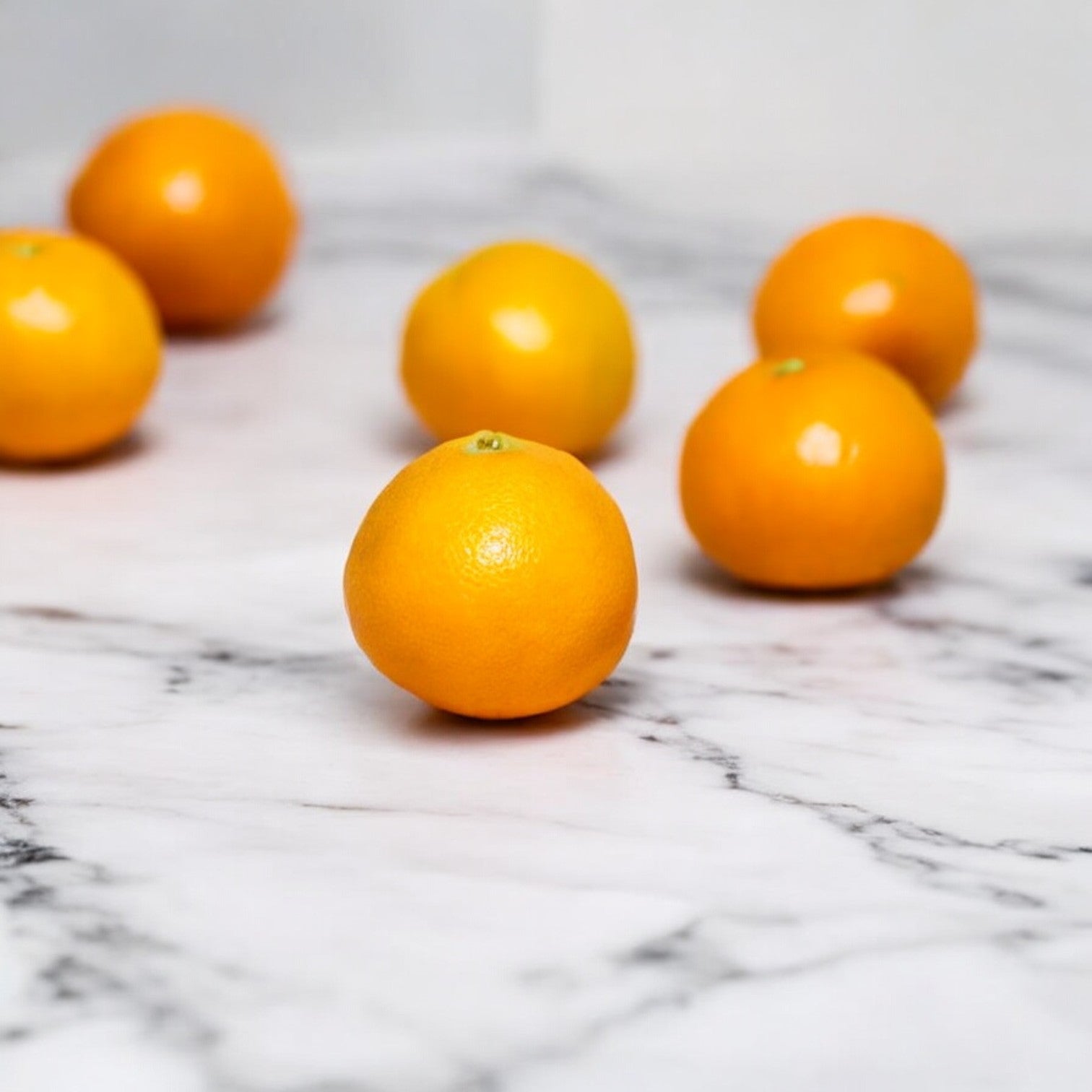 Six vibrant orange Cuties Organic mandarins from the Cuties brand are arranged on a white marble surface.