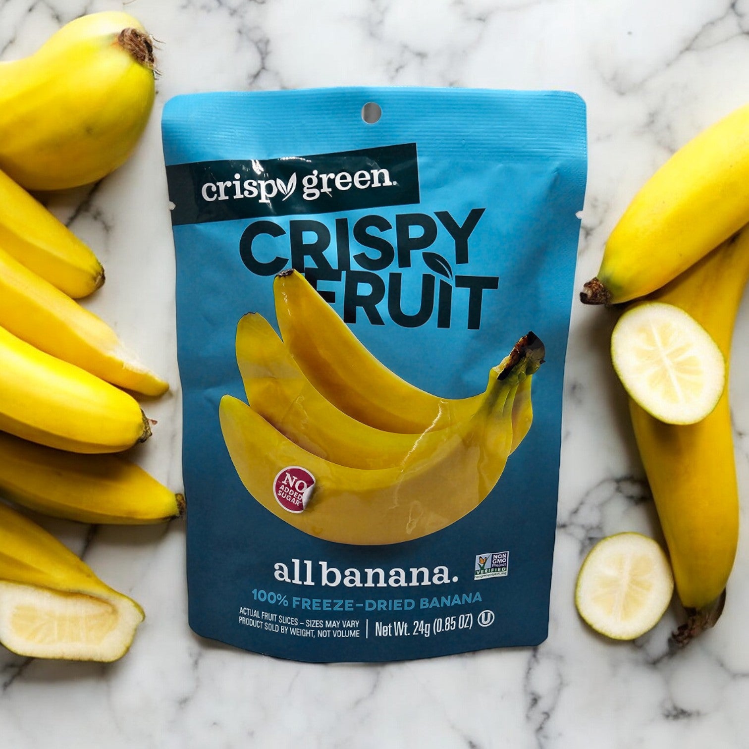 A package of Crispy Green Crispy Fruit All Banana - 0.35 oz - 1 Count with an authentic taste on a marble surface, surrounded by whole bananas.