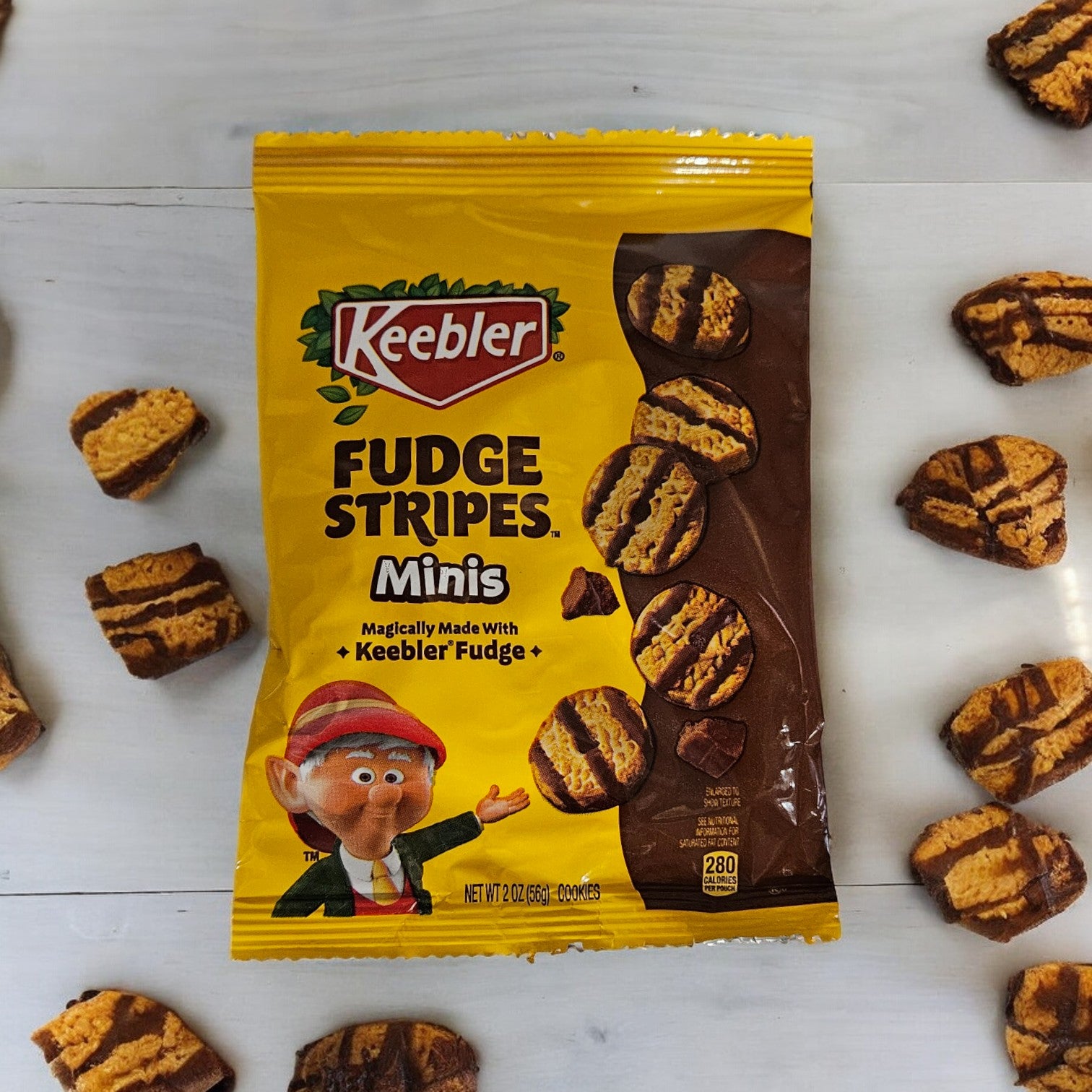 A yellow bag of Keebler Fudge Strips-2 oz - 1 Count, depicting an elf character and showcasing images of the buttery shortbread cookies coated in genuine Keebler fudge, is surrounded by several cookies.