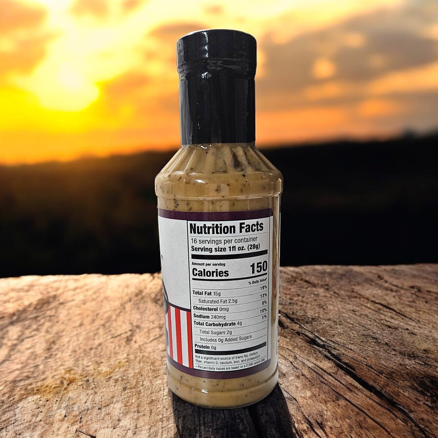 A Portillo's Bottle of Roasted Garlic Vinaigrette, 16 oz., with its nutrition facts label, rests on a wooden surface while an orange sunset casts a warm glow over the distant landscape.