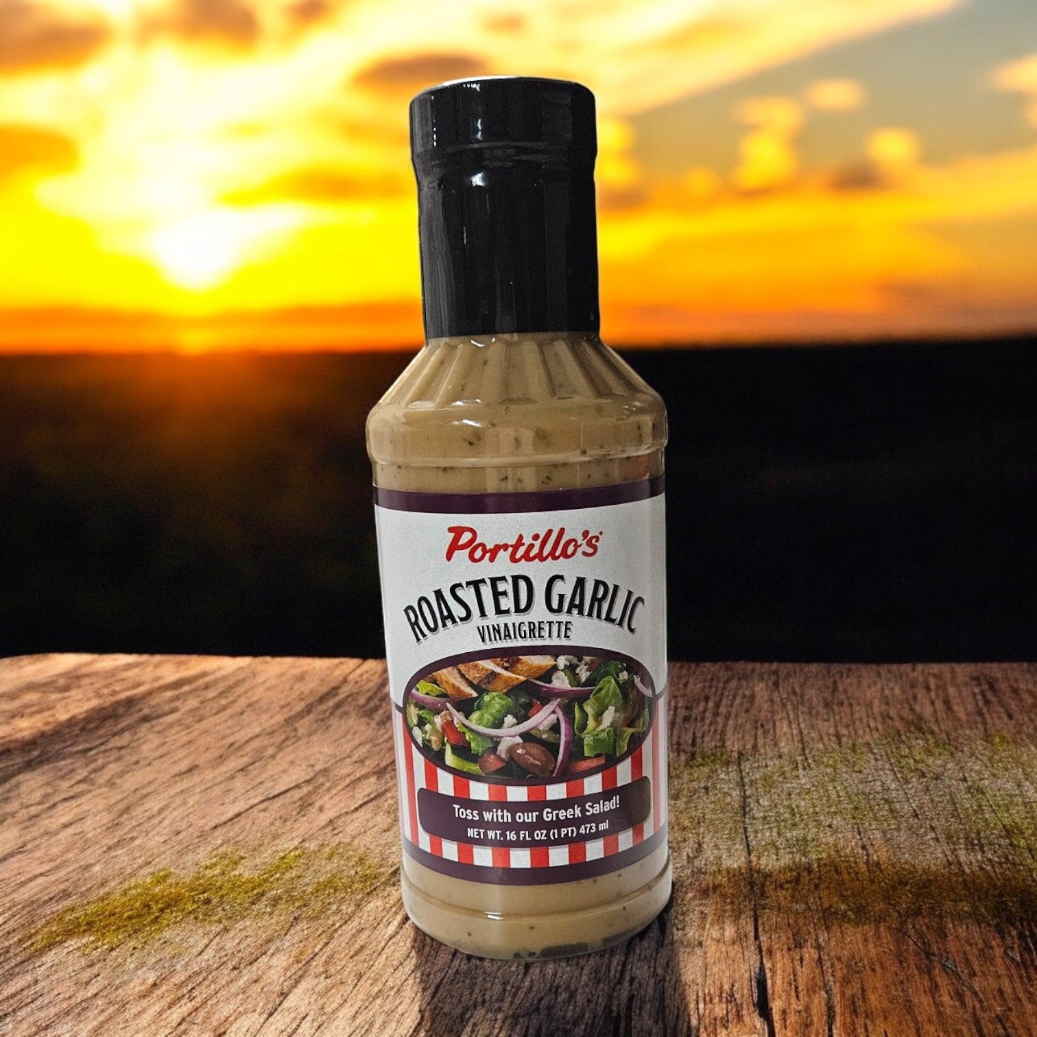 A 16 oz. Portillo's Bottle of Roasted Garlic Vinaigrette sits on wood, bathed in the warm glow of a blurred sunset.