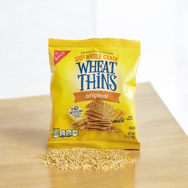 A bag of Wheat Thins 1.75 oz sits on a wooden surface, with some loose wheat grains in front of the bag—perfect for a healthy snack.