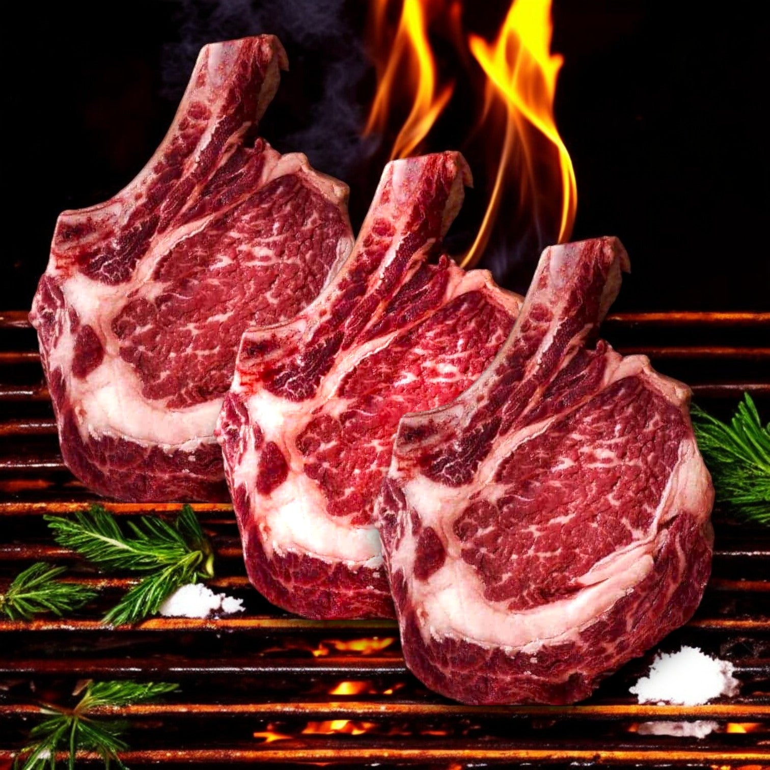 Three Mino Prime Steaks, 22 oz "Aleck Cut" Cowboy Ribeyes sizzle on the grill, flames dancing in the background, garnished with herbs and salt.