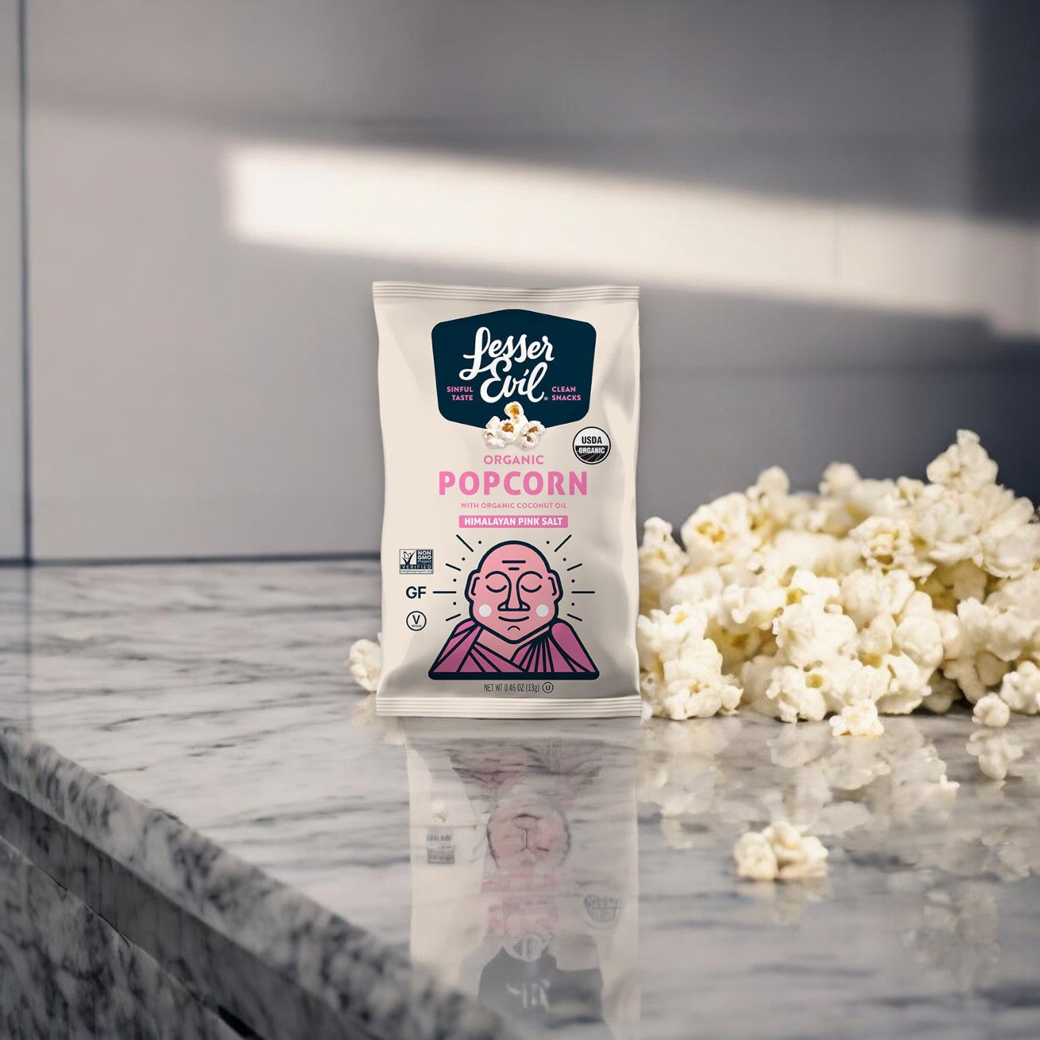 A bag of LesserEvil Organic Popcorn, Snack Pack, Himalayan Pink (0.46 oz), a healthy snack, is placed on a marbled surface, with some loose popcorn scattered next to it.