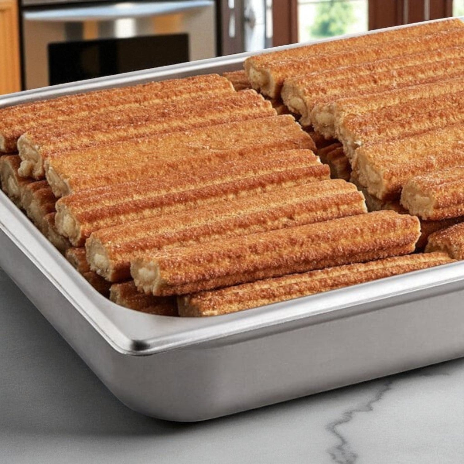 A metal tray displays rows of Sabor Nuestro Frozen Bavarian Cream-Filled Churros, 10" (50 ct), on a marble countertop in the kitchen.