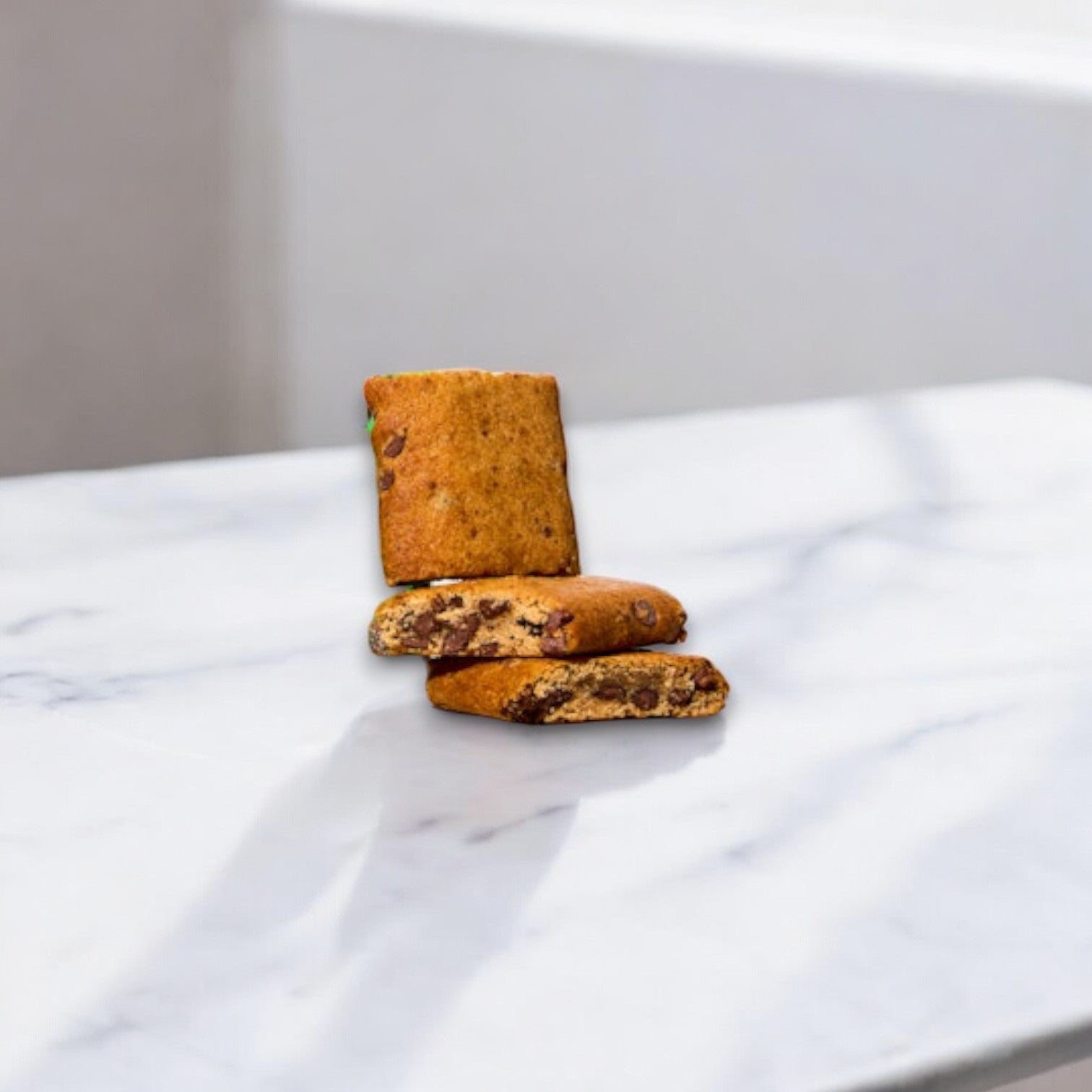 Three LÄRABAR Kid Gluten Free Chocolate Chip Cookie Bars, each 1.6 oz, are stacked irregularly on a white marble surface, showcasing a wholesome and nutritious snack that aligns with clean eating principles.