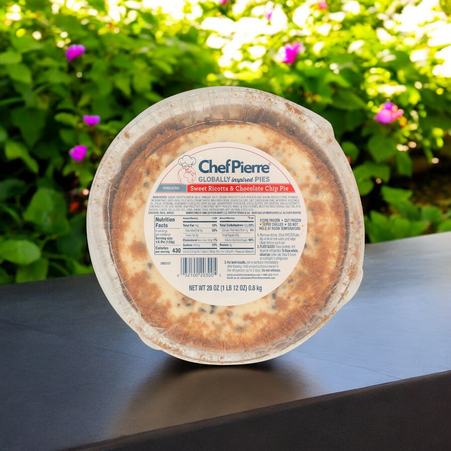 The Chef Pierre Sweet Ricotta and Chocolate Chip Pie (10", 6/28 oz) rests on a table, its buttery flavors wafting through the air against a blurred garden background, evoking a classic dessert setting.