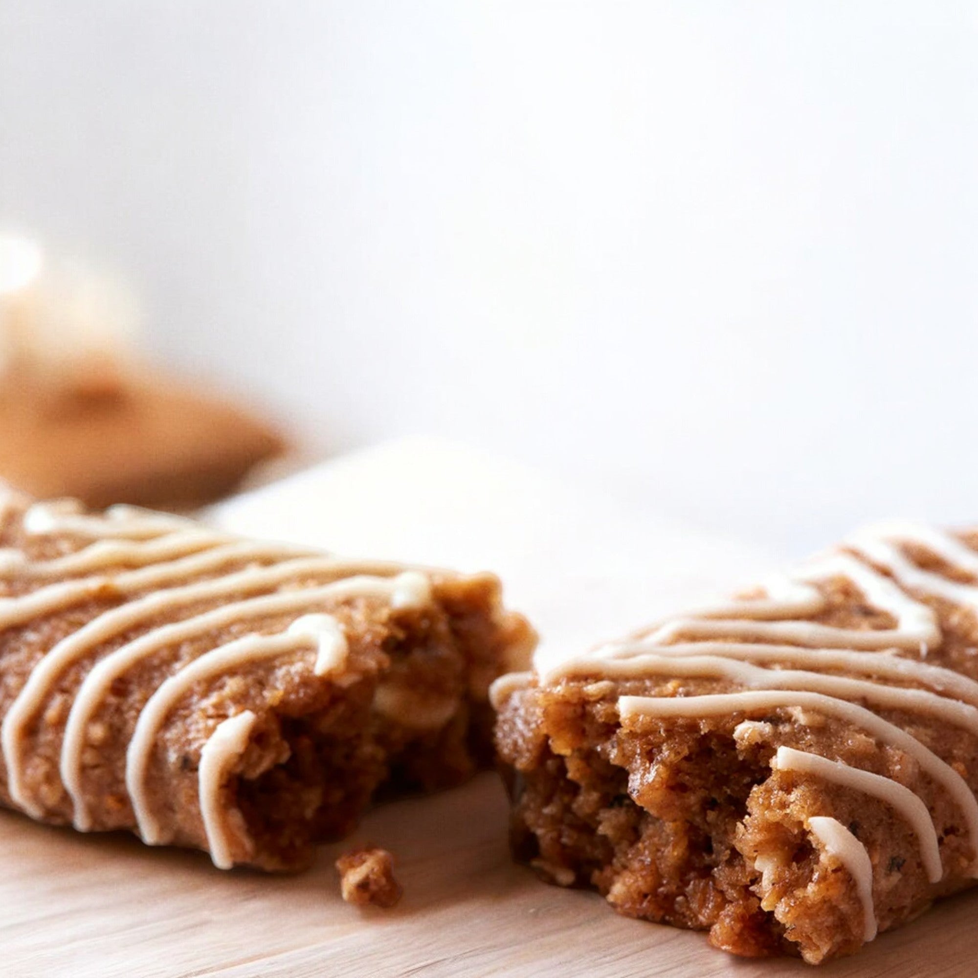 Close-up of two halves of a Clif Kid Zbar Organic Iced Oatmeal Cookie Snack Bar with a visible brown sponge texture and white icing drizzled on top, made with organic ingredients, and perfect for kids snack bars, placed on a light wooden surface.