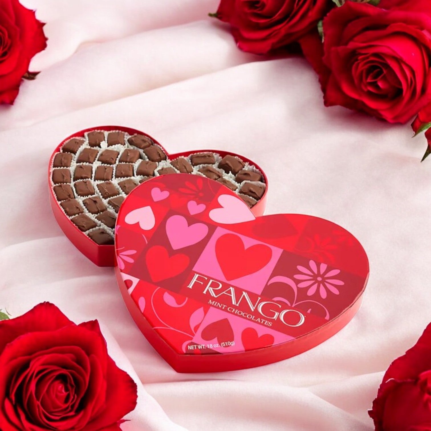 A Valentine's Day scene features a Macy's Frango Chocolates Heart Milk Mint Box, 18 oz, surrounded by red roses on soft pink fabric.