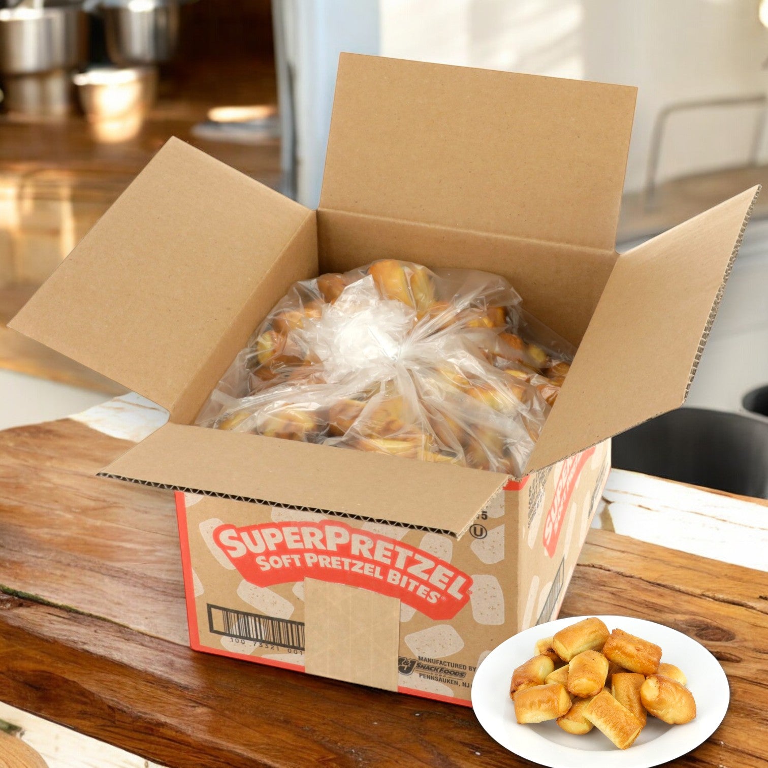 A box of bite-sized pretzels rests on a wooden table, and in front, a white plate presents the delightful SUPERPRETZEL Soft Baked Pretzel Bites from Super Pretzel.