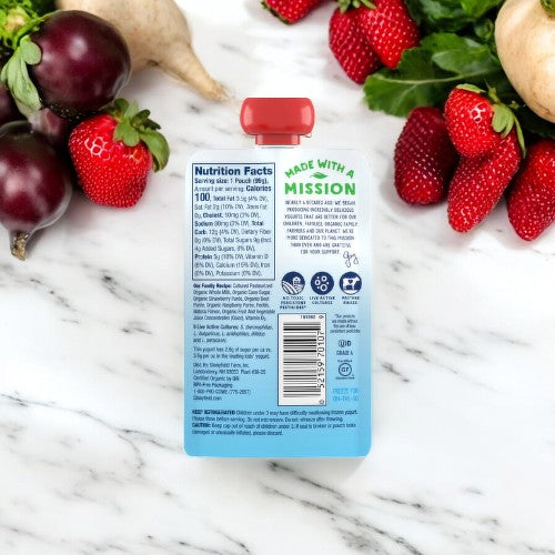 Stonyfield's Organic Strawberry Beet Berry Kids' Yogurt pouch on a marble counter with eggplants, mushrooms, and organic strawberries. The pouch displays nutritional information and reads "Made with a mission. Infused with live active cultures and packed with vitamin D3.