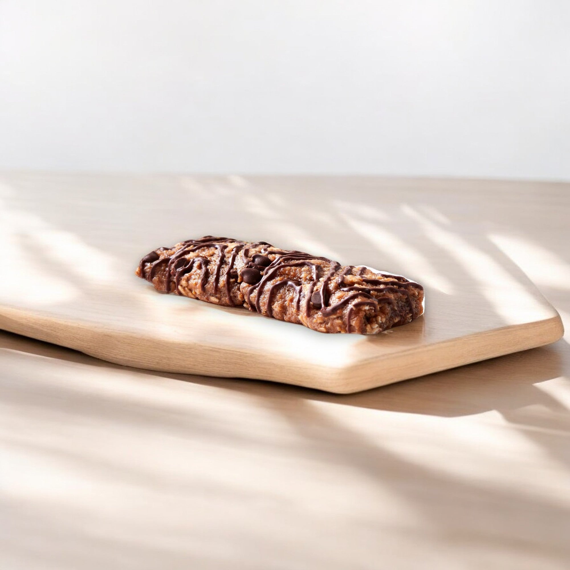 A Clif Bar Z Bar Chocolate Chip, packed with whole grains, sits on a light wooden cutting board with a plain background—perfect for on-the-go snacking.