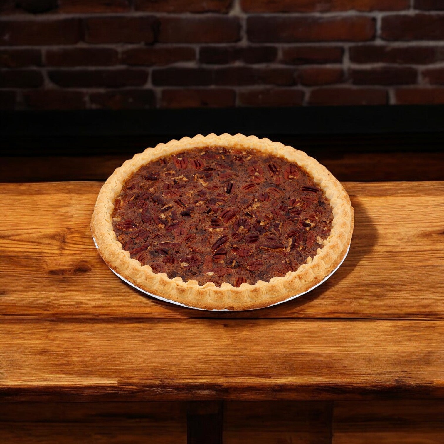 A Chef Pierre Southern Pecan Pie sits on a wooden table against a rustic brick wall, its pecan filling invitingly rich and smooth.