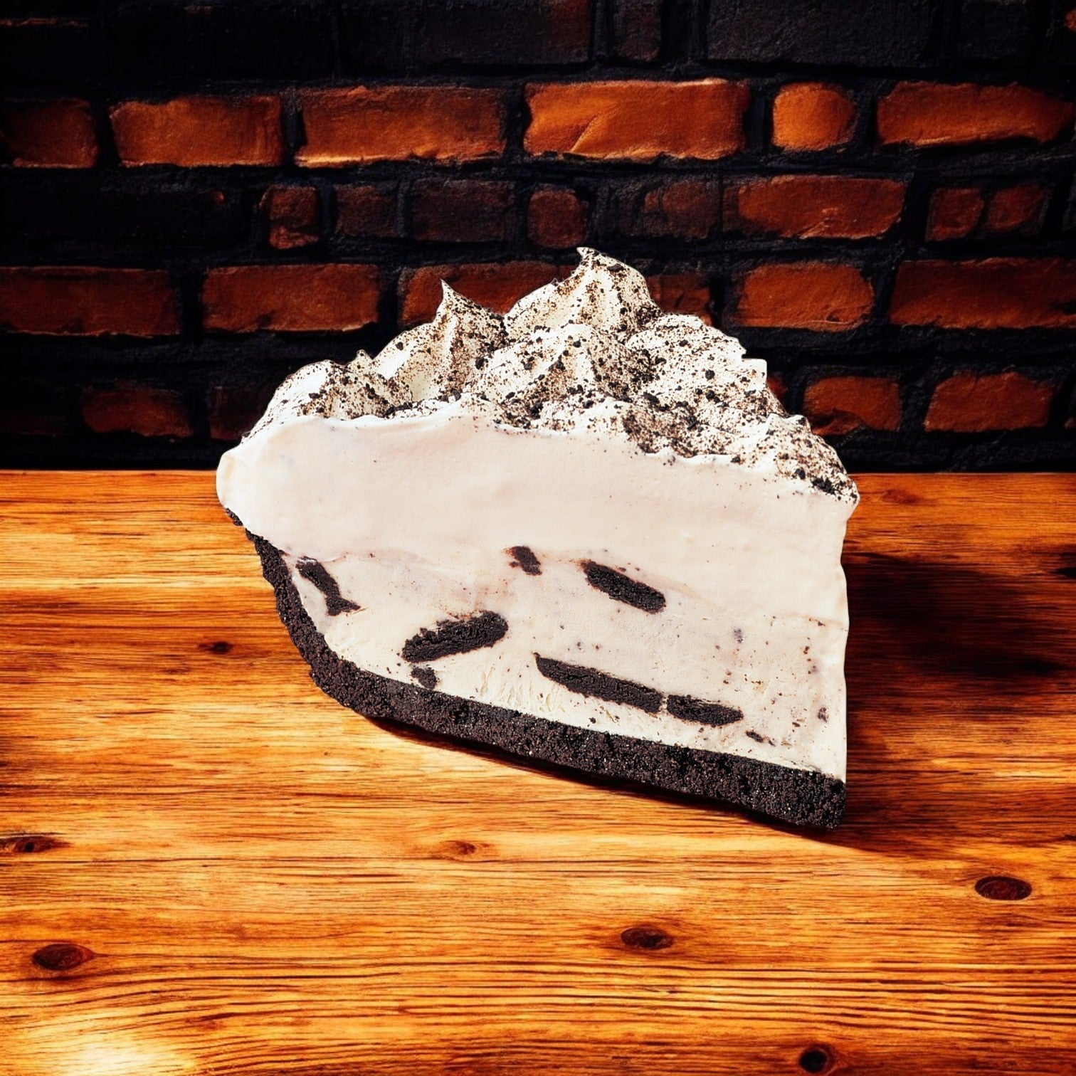 A slice of Sysco's Cookies & Cream Pie, an indulgent treat with Oreo chunks, rests on a wooden surface against a brick wall, satisfying any dessert craving.