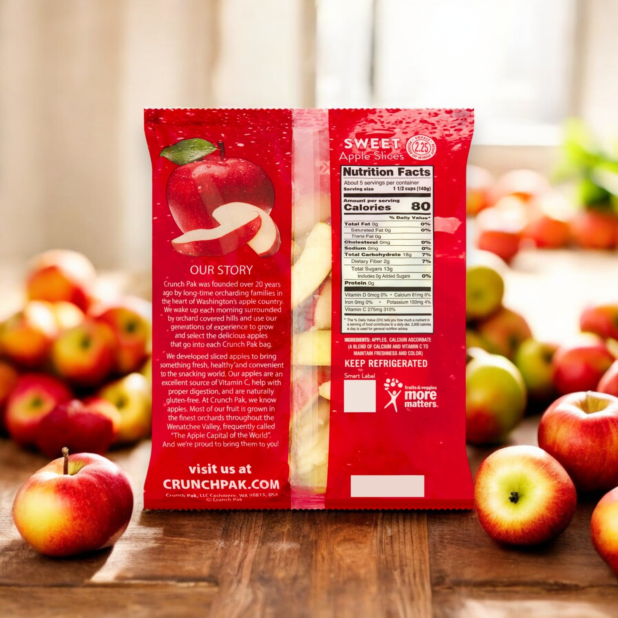 The back of a Crunch Pak Fresh Sweet Apple Slices, Family Size, 24oz Resealable Bag pack rests on a wooden table with scattered apples. The text shares the company's story along with nutrition facts and storage instructions. The red packaging adorned with apple graphics makes these Crunch Pak Sweet Apple Slices ideal for healthy, on-the-go snacking.