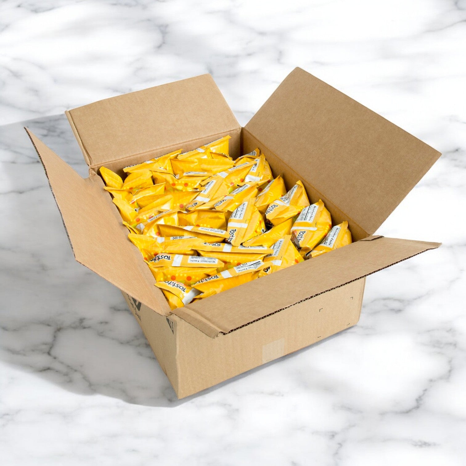 An open cardboard box rests on a marble surface, full of individually packaged yellow treats—each offering a delicious hint of Tostitos Tortilla Chips, Round.